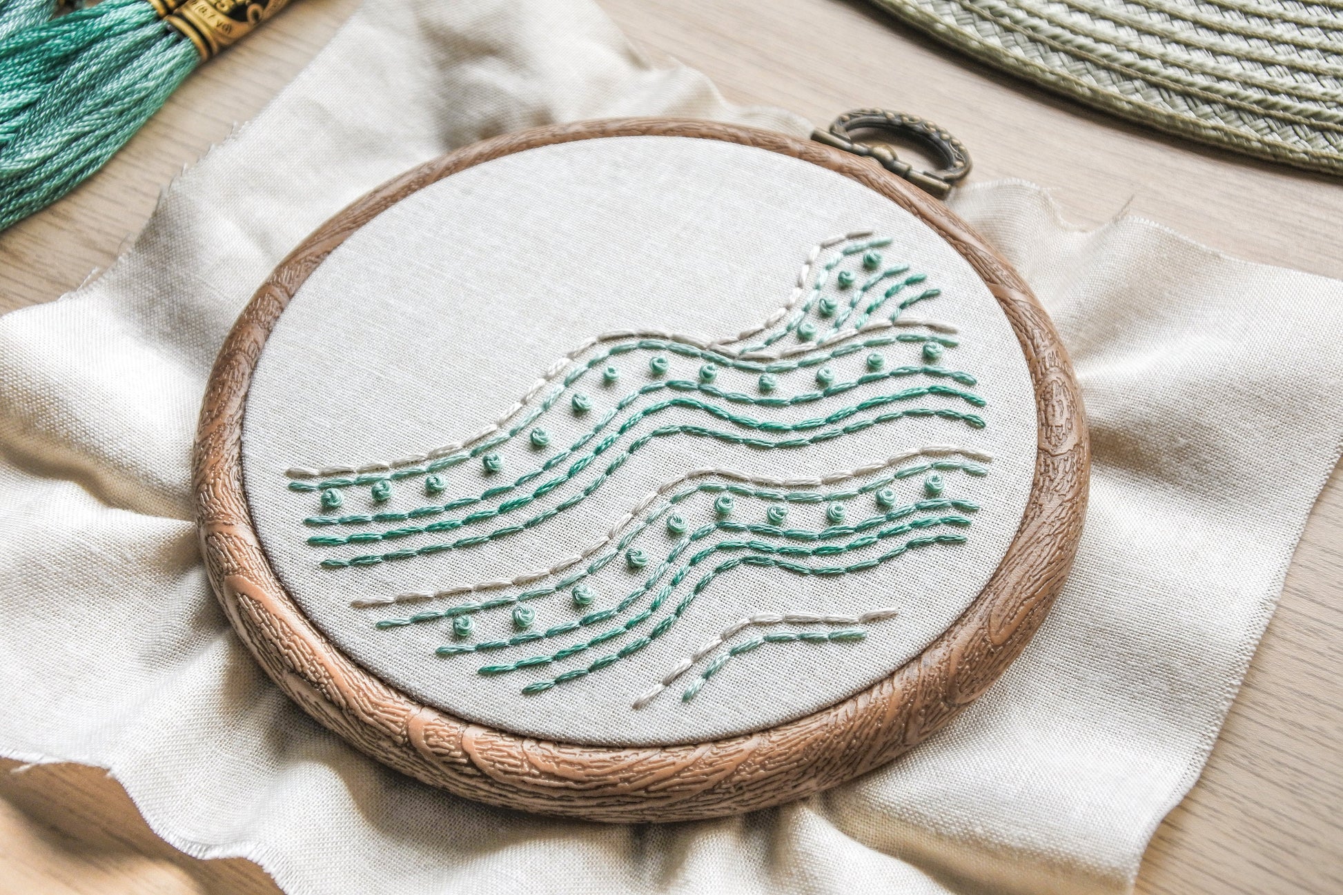Angled closeup of turquoise and white backstitch and French knots in the beach wave embroidery pattern