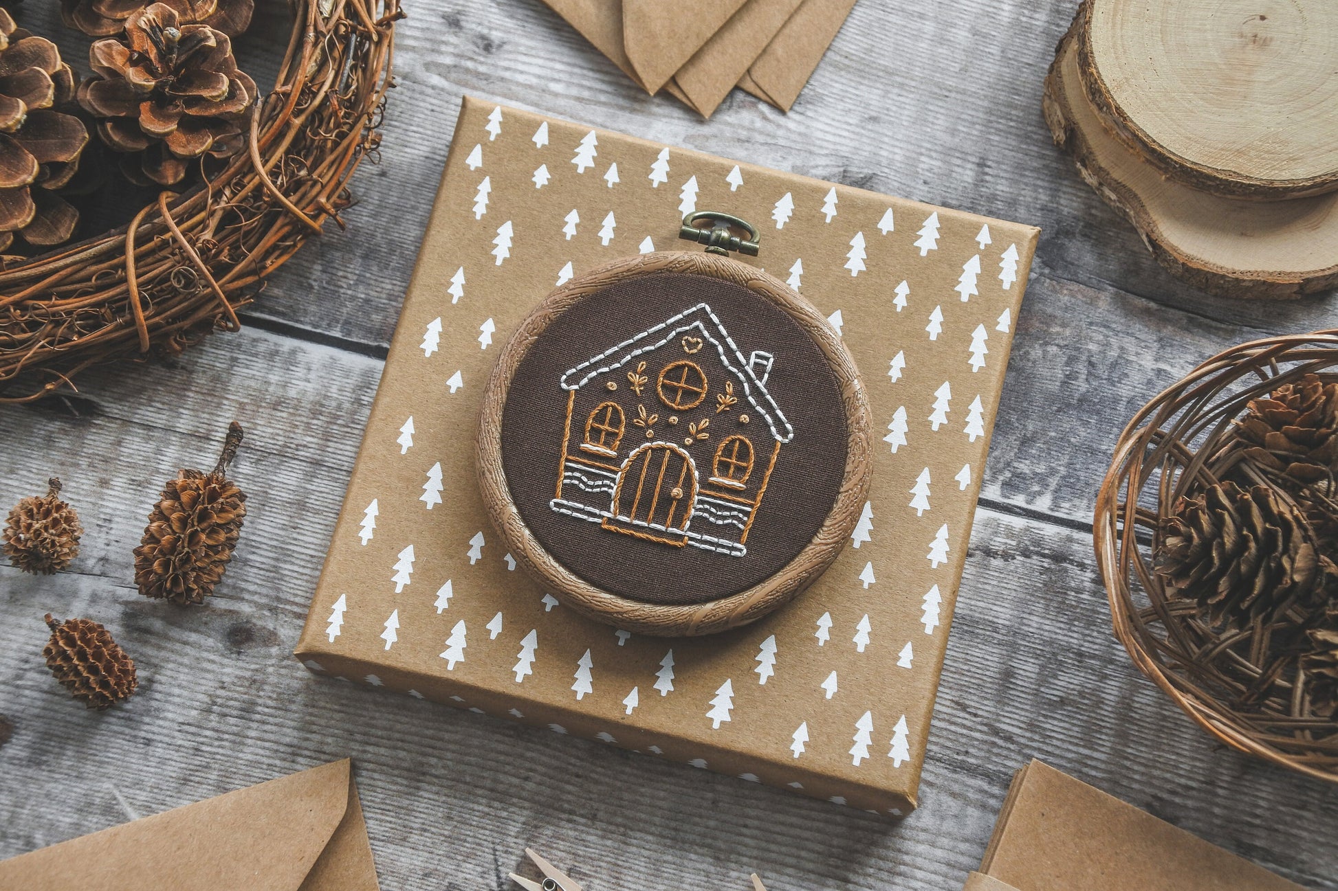 Angled view of hand-embroidered gingerbread house design in wood effect hoop, showcasing stitching details on brown fabric.