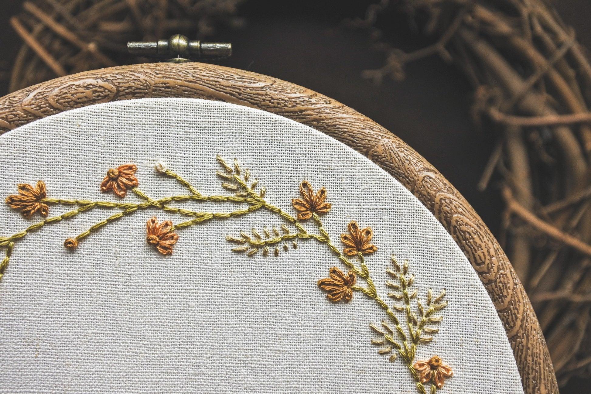 Closeup of embroidered leaves, grass and coneflowers in a warm autumn colour palette on a neutral fabric background.