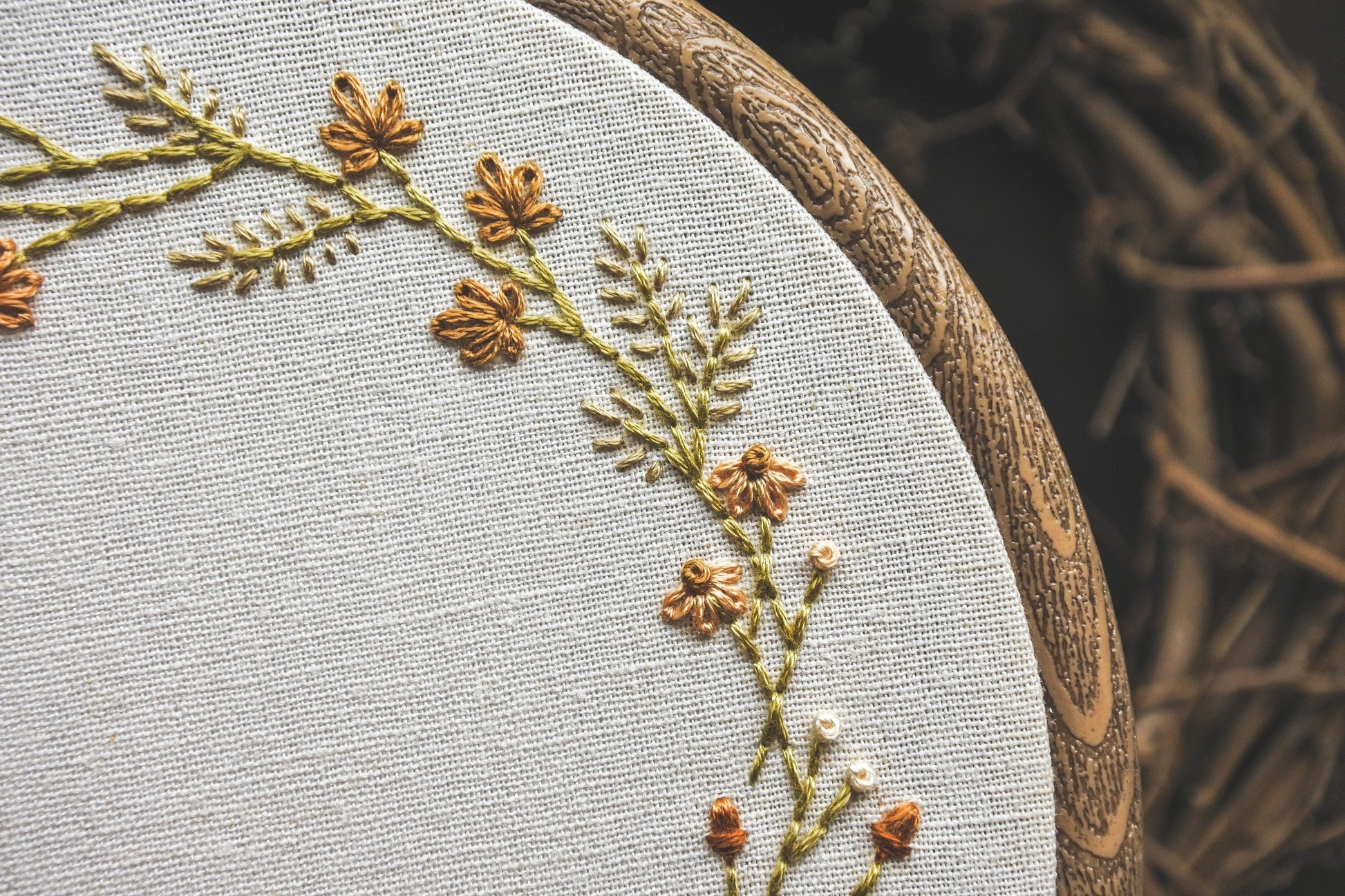 Closeup of hand embroidered acorns, leaves, grasses and flowers with warm seasonal tones, part of a custom name embroidery hoop design.
