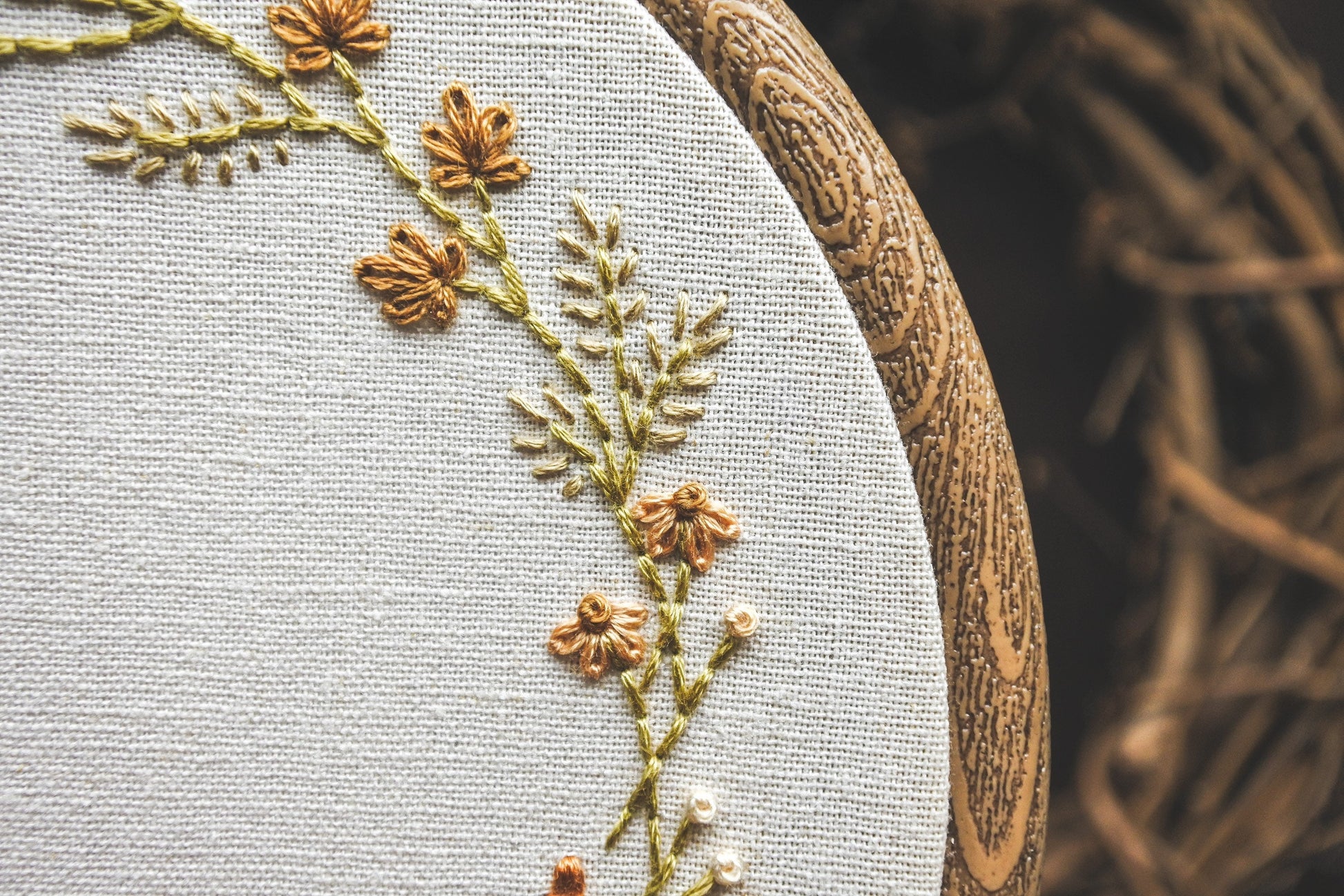 Detailed view of hand stitched autumn leaves and coneflowers in warm golden brown shades, part of a personalised name embroidery hoop.