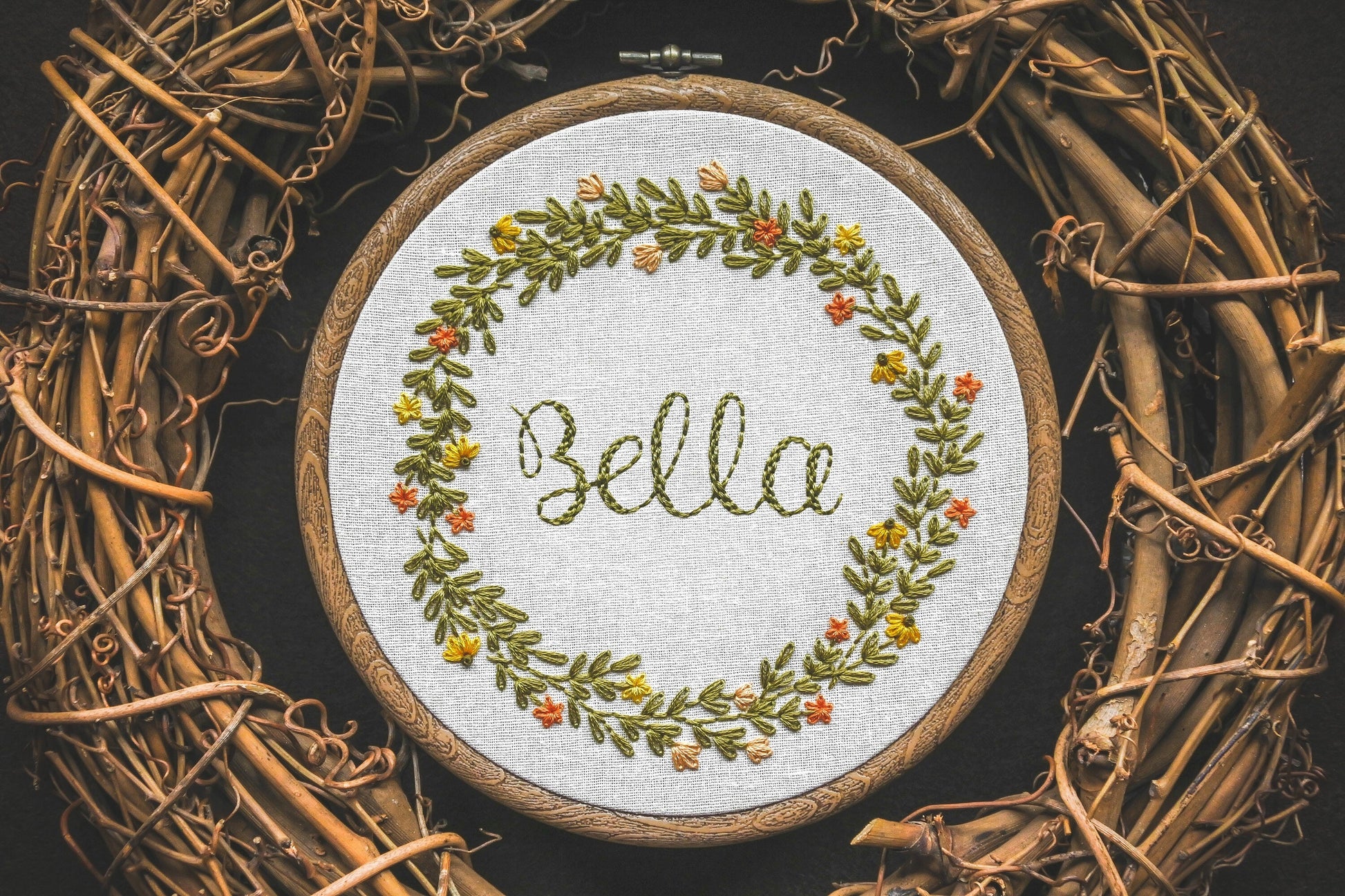 Hand embroidered summer wreath name hoop with the name Bella stitched in the centre, surrounded by orange and yellow flowers with lush greenery
