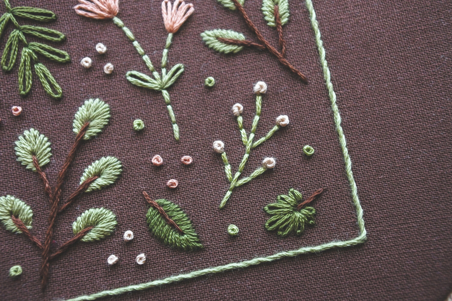 Close-up of soft spring-toned floral and botanical embroidery details on dark brown fabric, showcasing intricate stitching 