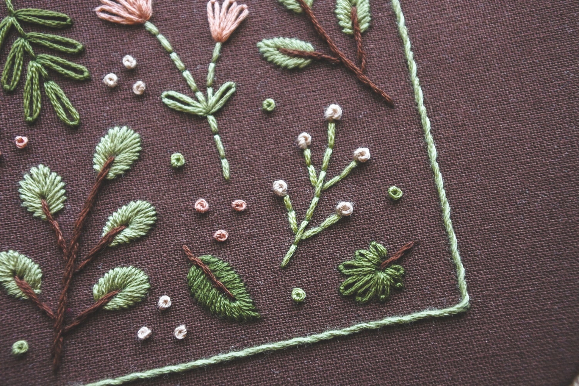 Close-up of soft spring-toned floral and botanical embroidery details on dark brown fabric, showcasing intricate stitching 