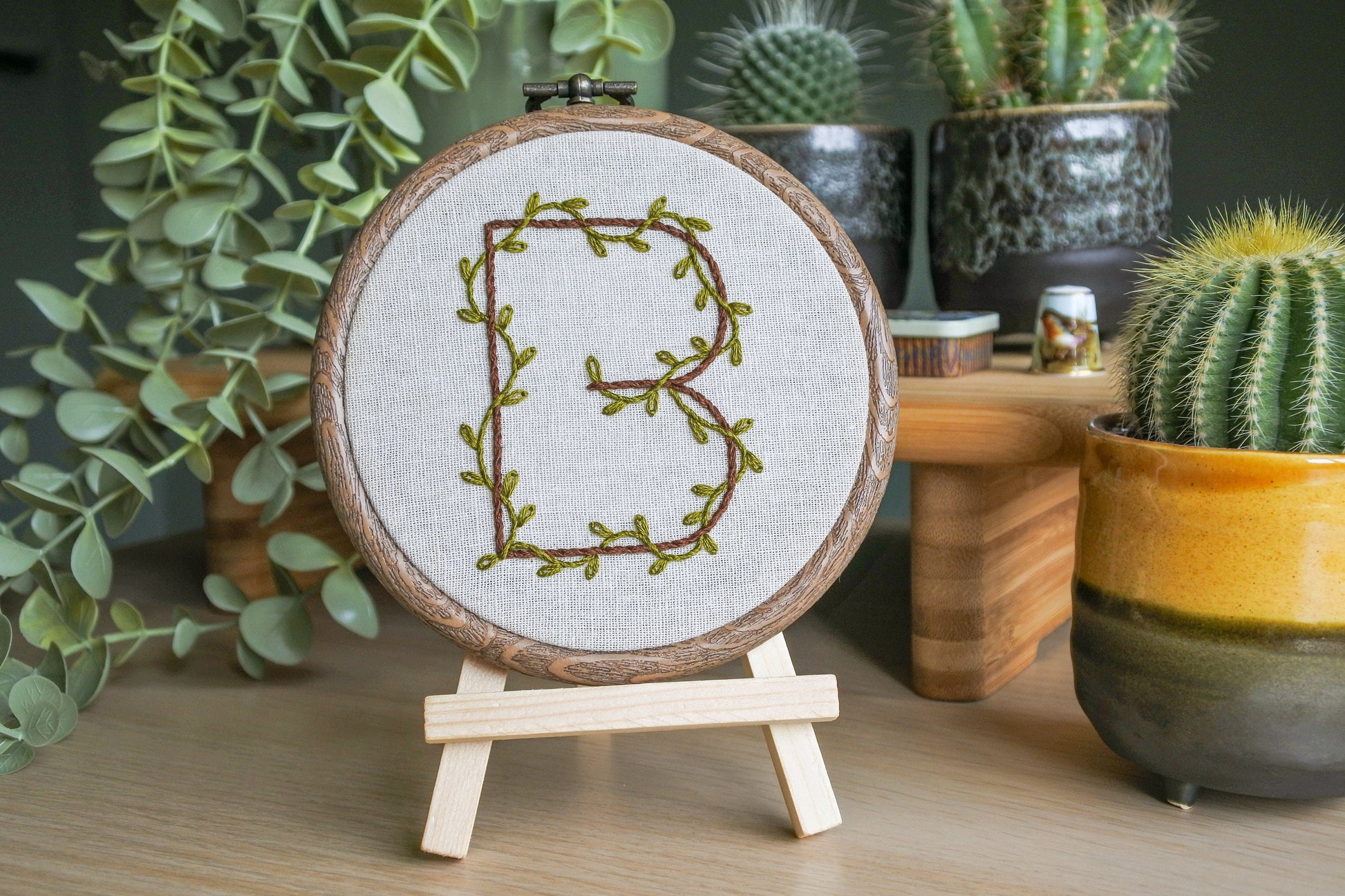 Hand embroidered letter b in a wood effect hoop displayed on a mini wooden easel.