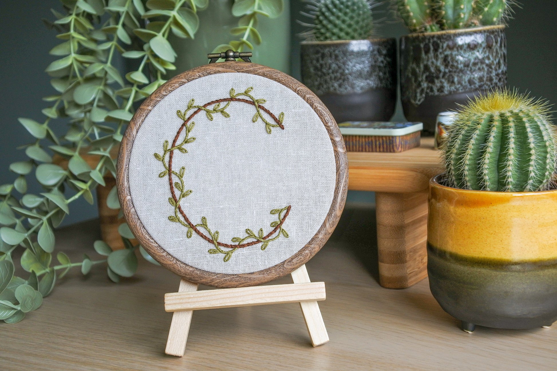 Botanical letter C embroidery hoop with green vines and brown letter displayed on a small wooden easel
