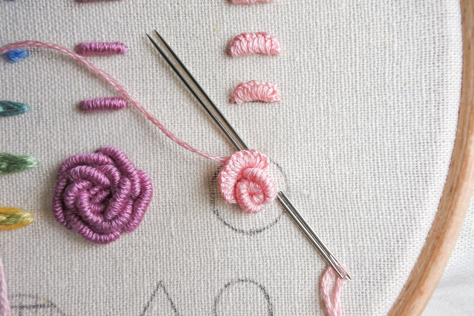 Progress photo of cast-on stitch creating a textured rose with light pink thread on fabric. Also shows other variations of stitches like Bullion stitch in purple thread.