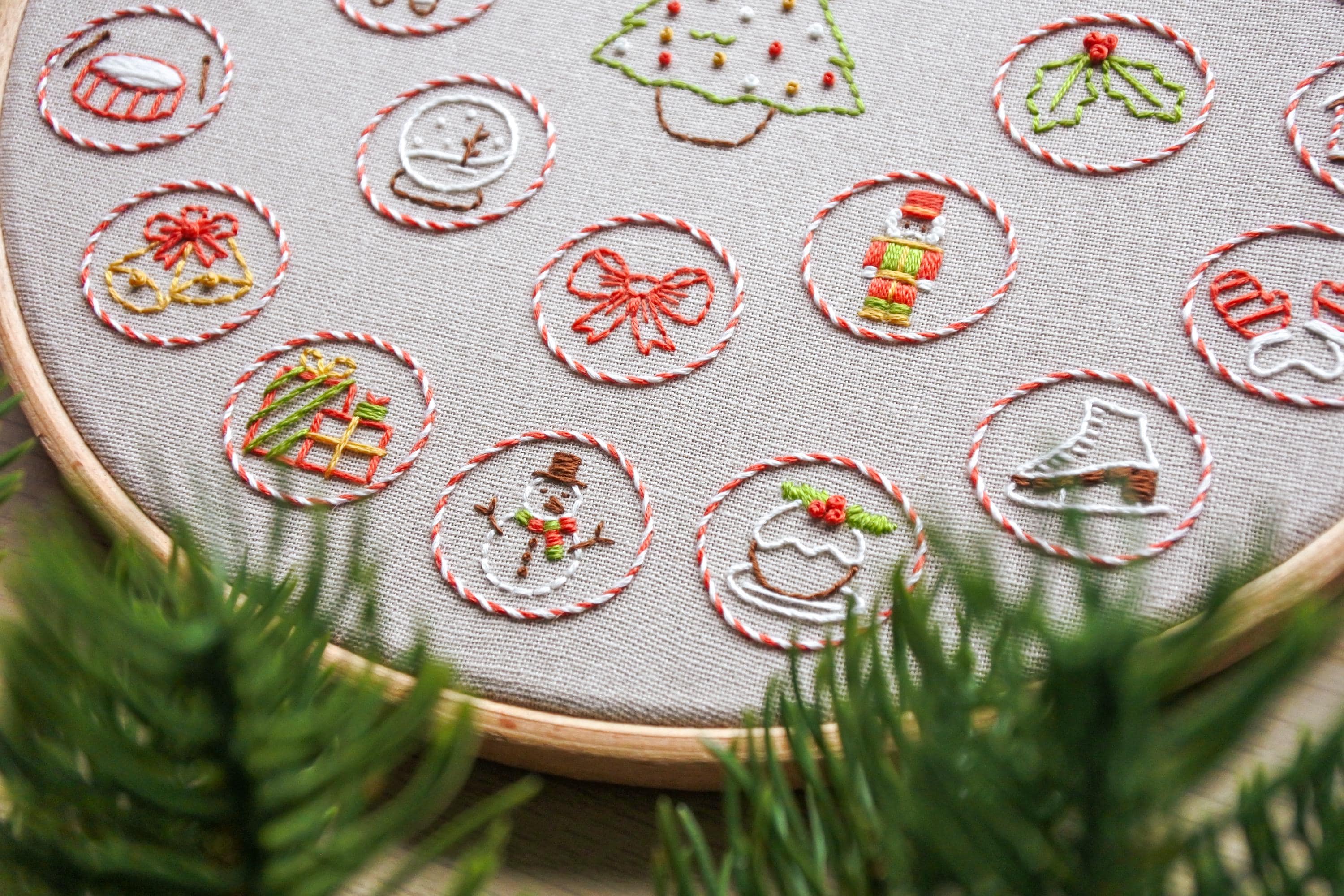 Close-up of hand embroidered mini festive elements on Christmas advent calendar hoop, including presents, a snowman, and snow globe.