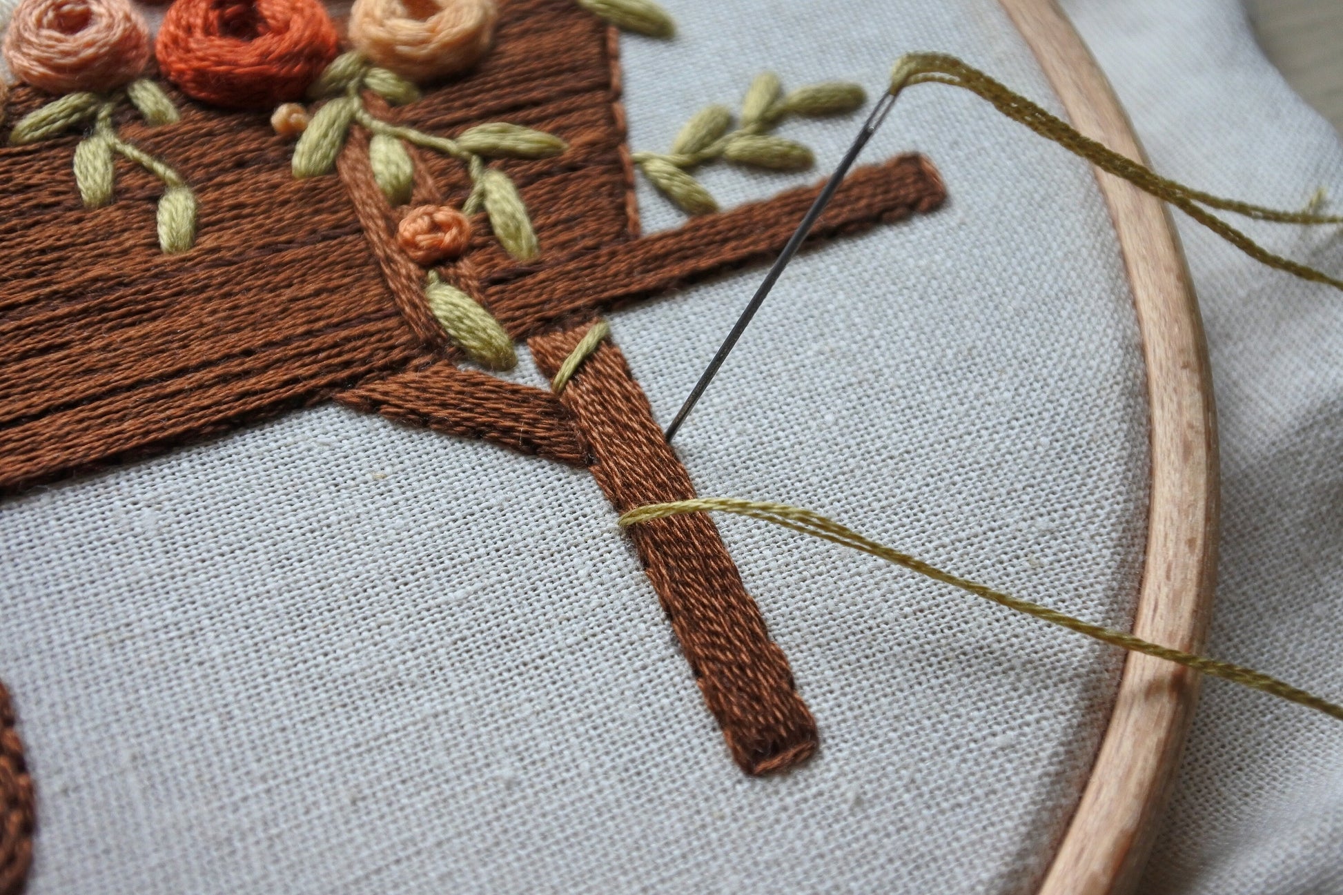 Close-up of needle and thread stitching the vine around the leg of the wagon on the autumn embroidery pattern