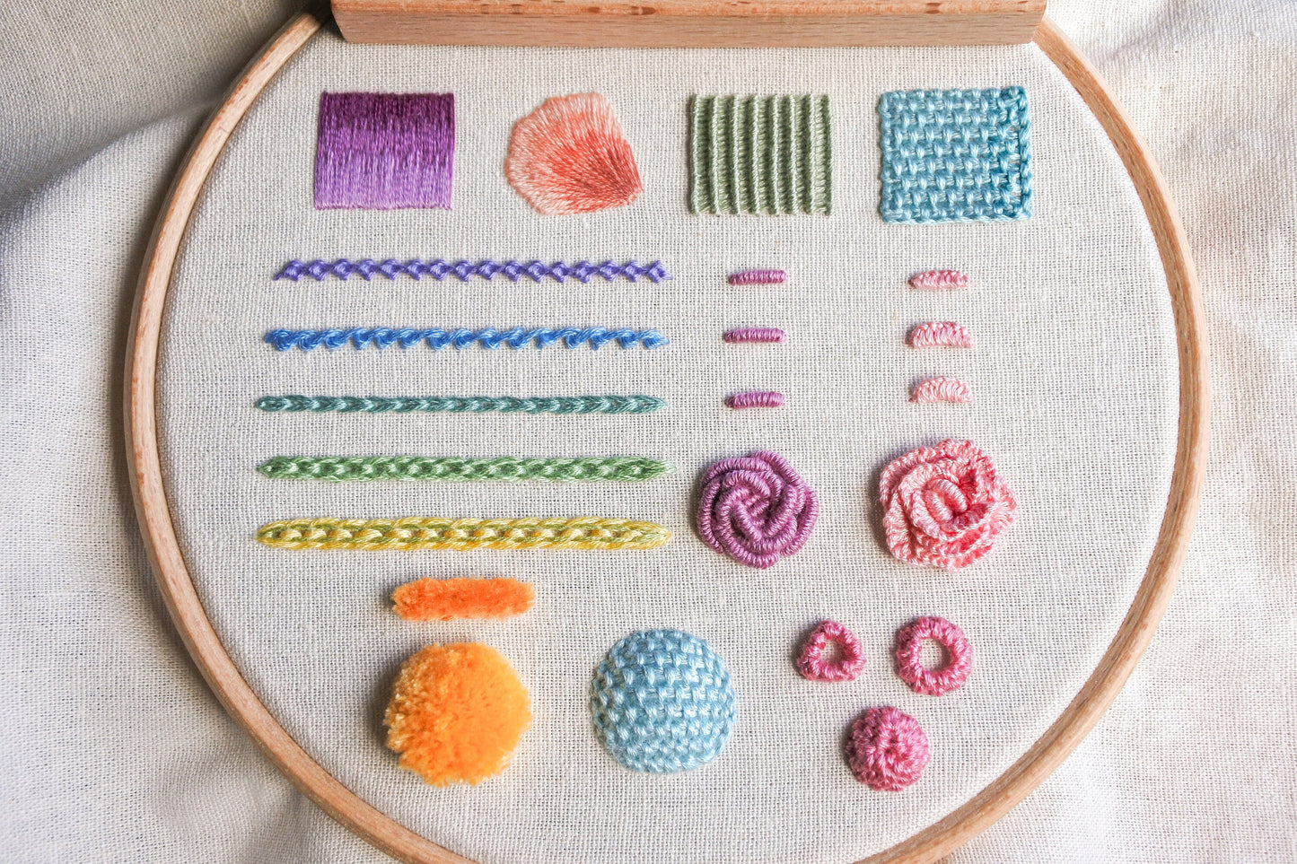 Finished hand embroidery stitch sampler featuring 12 colourful textured stitches on fabric in a wooden hoop