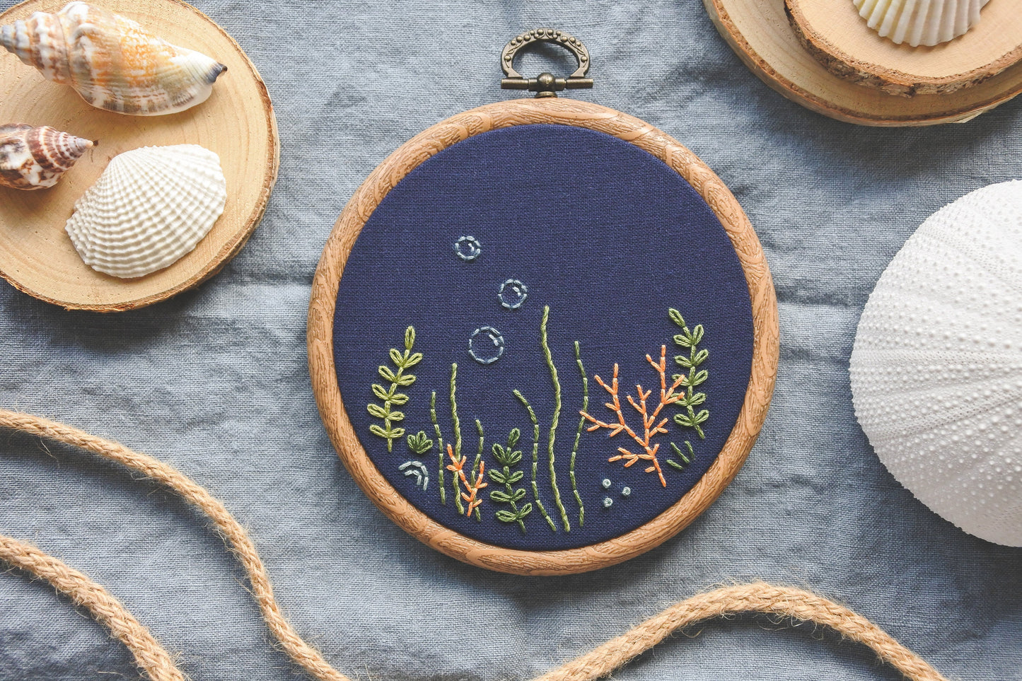 Hand-embroidered coral reef design in wood effect hoop, stitched on navy blue fabric