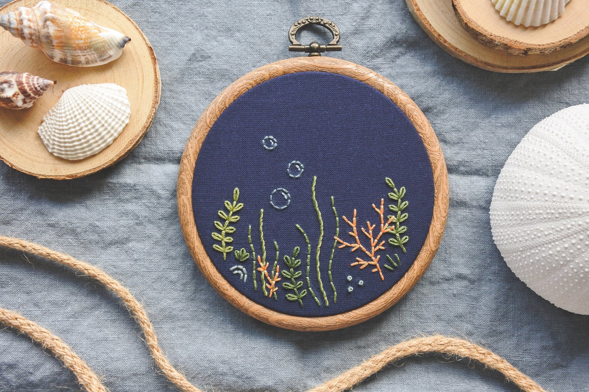 Hand-embroidered coral reef design in wood effect hoop, stitched on navy blue fabric