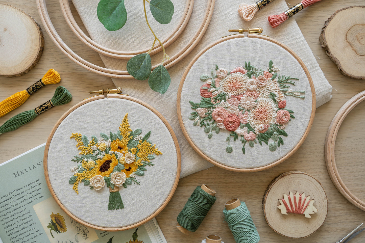 Two hand-embroidered floral bouquet hoops, one featuring sunflowers and roses with a yellow and white colour scheme, the other with dahlias and roses in soft pinks and creams, both with eucalyptus leaves