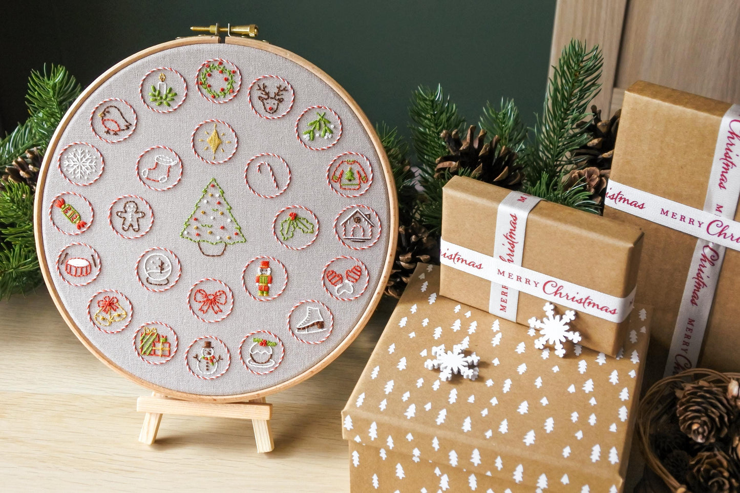 Advent calendar embroidery hoop displayed on a mini wooden easel next to christmas presents.