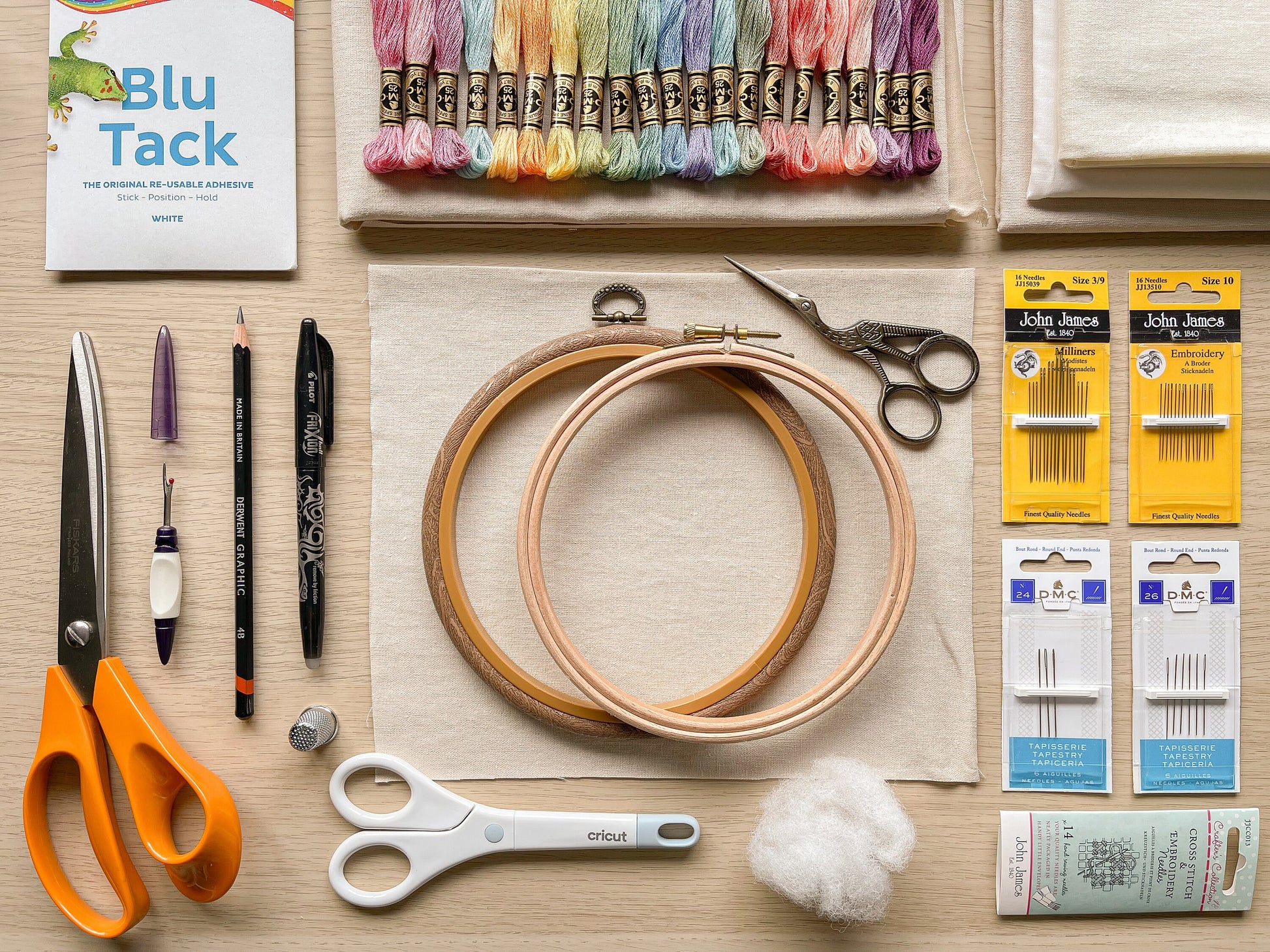 Flatlay of embroidery supplies including threads, needles, fabric, and an embroidery hoop for the stitch sampler