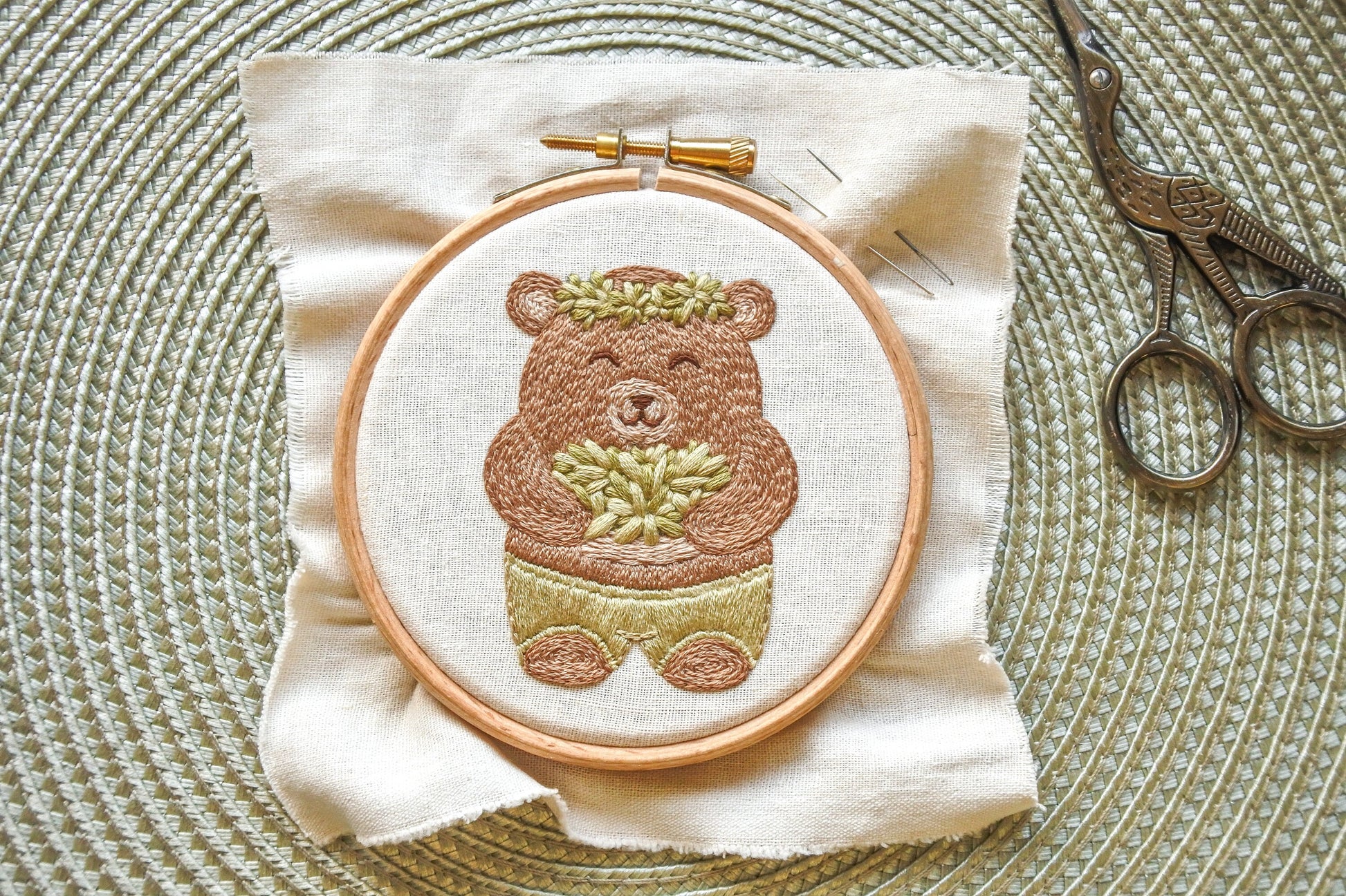 Finished bear embroidery design in hoop on neutral fabric, with fabric edge visible before backing.