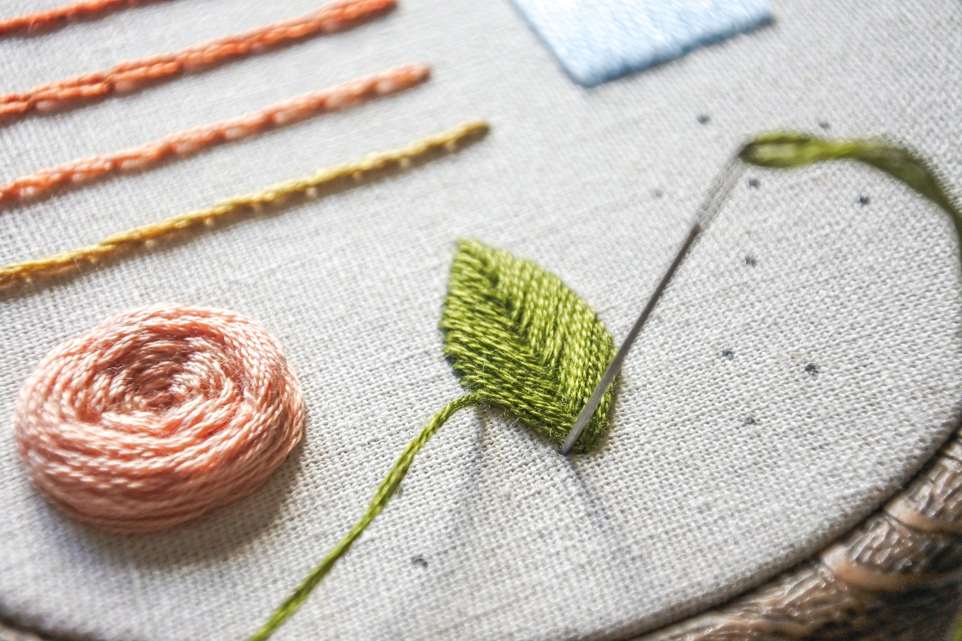 Close-up of needle stitching a green leaf using the fishbone stitch on fabric