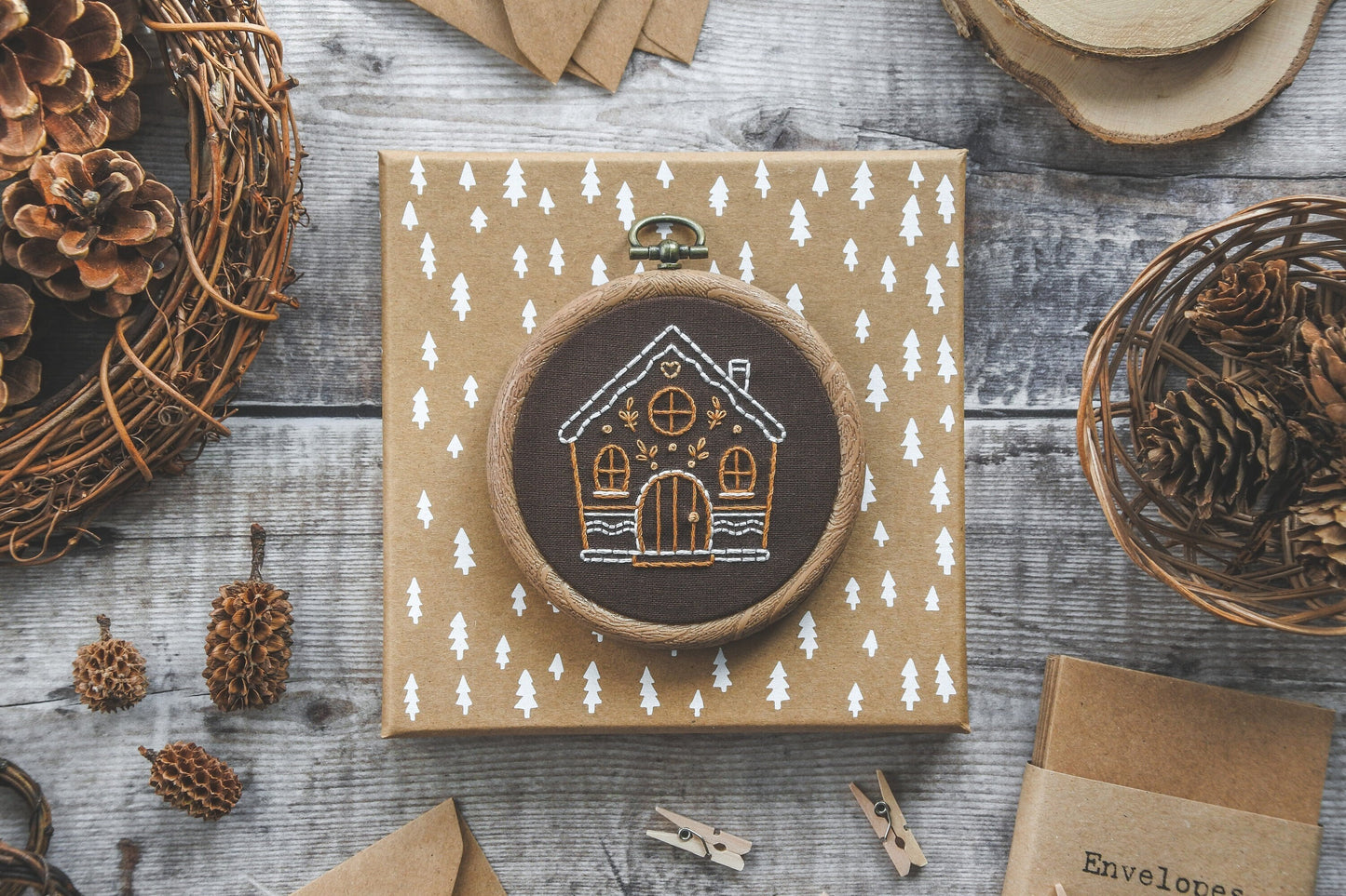 Flatlay of hand-embroidered gingerbread house design on brown fabric.