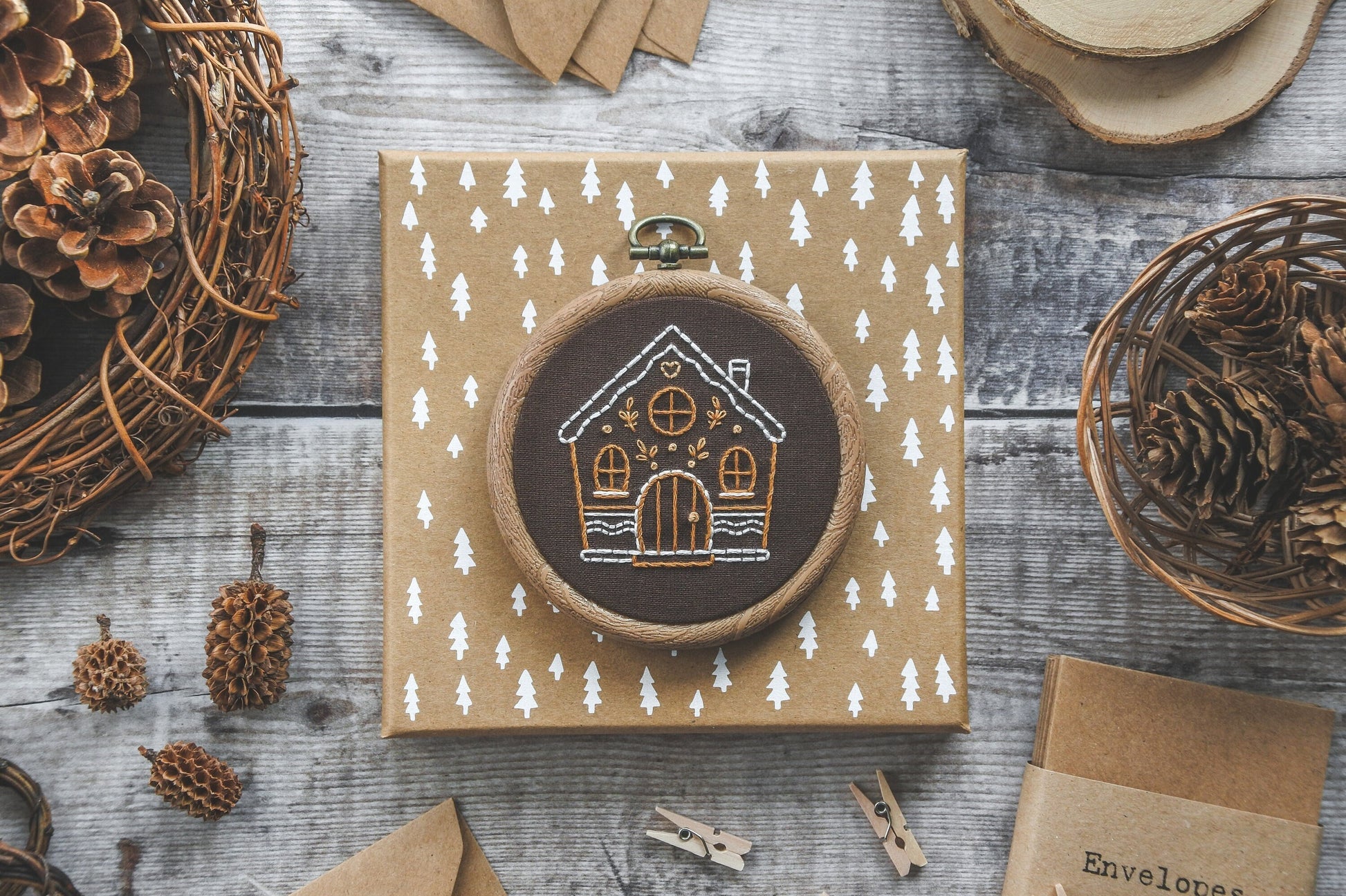 Flatlay of hand-embroidered gingerbread house design on brown fabric.