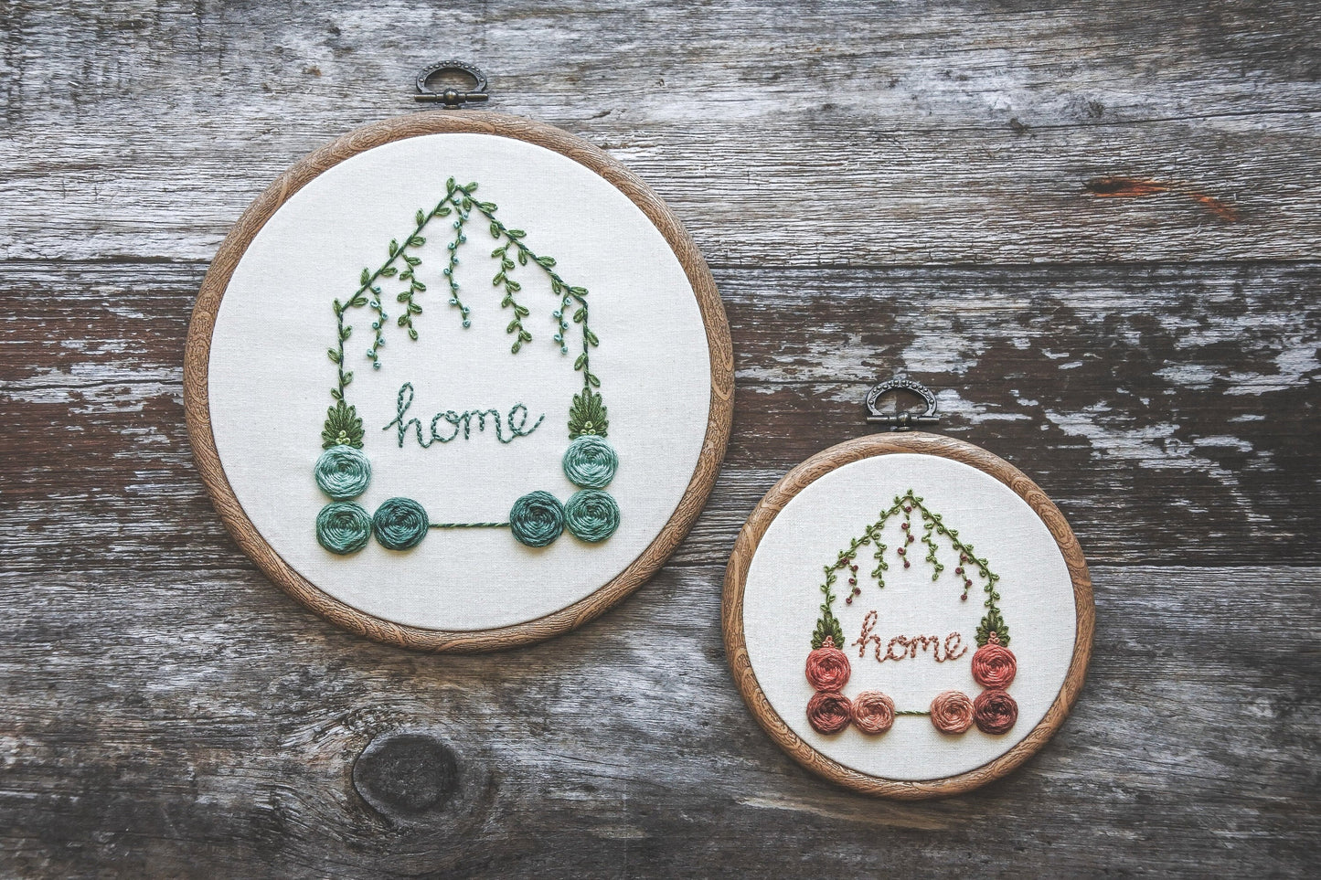 Two hand-embroidered floral home hoops – one 6-inch with turquoise colours and one 4-inch with red and peach colours, both with green foliage.
