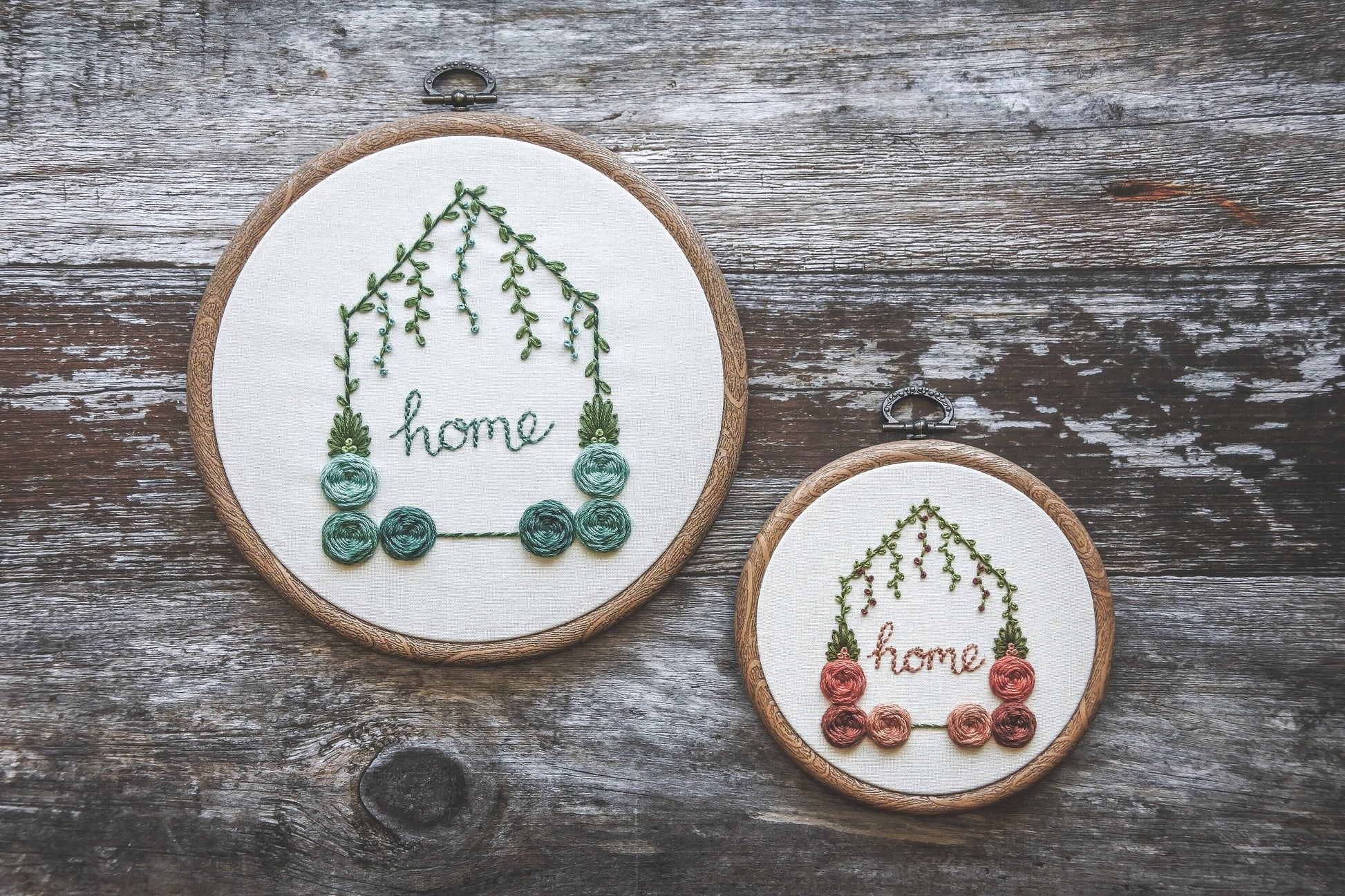 Two hand-embroidered floral home hoops – one 6-inch with turquoise colours and one 4-inch with red and peach colours, both with green foliage.