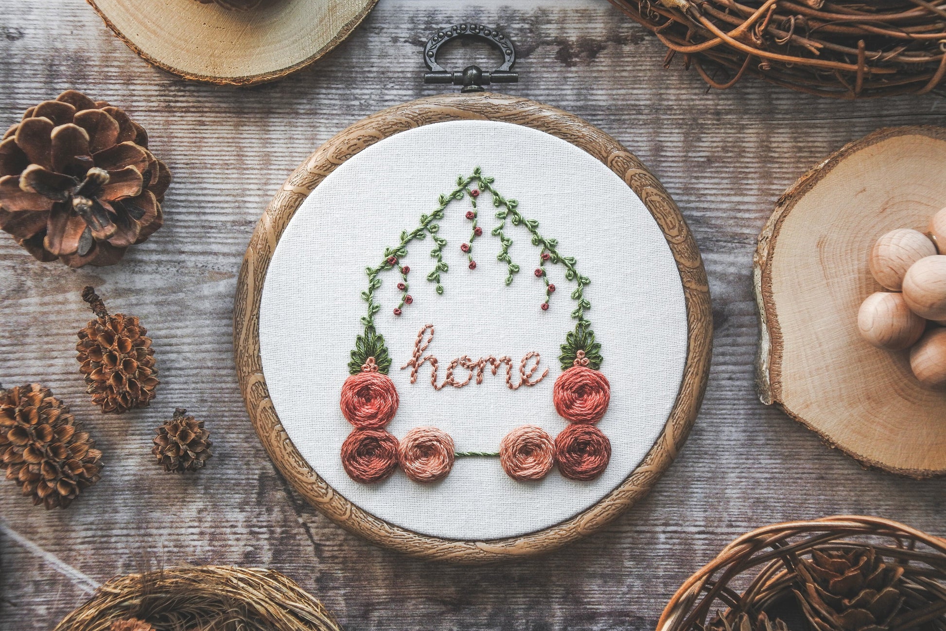 Hand-embroidered floral home hoop with red and peach colour scheme, green foliage, and the word 'home' in the centre.