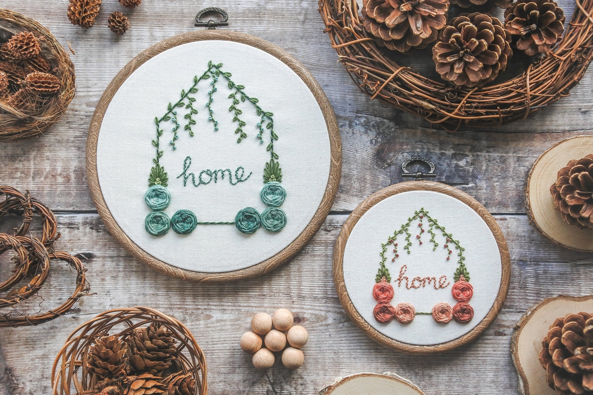 Two hand-embroidered floral home hoops with – one 6-inch personalised with turquoise colours, and one 4-inch with muted reds and peaches, both with green foliage.