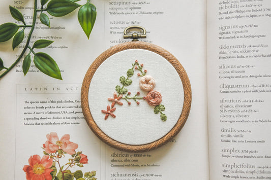 Hand-embroidered floral letter A hoop featuring peach flowers and green foliage in a 3-inch wood-effect hoop.