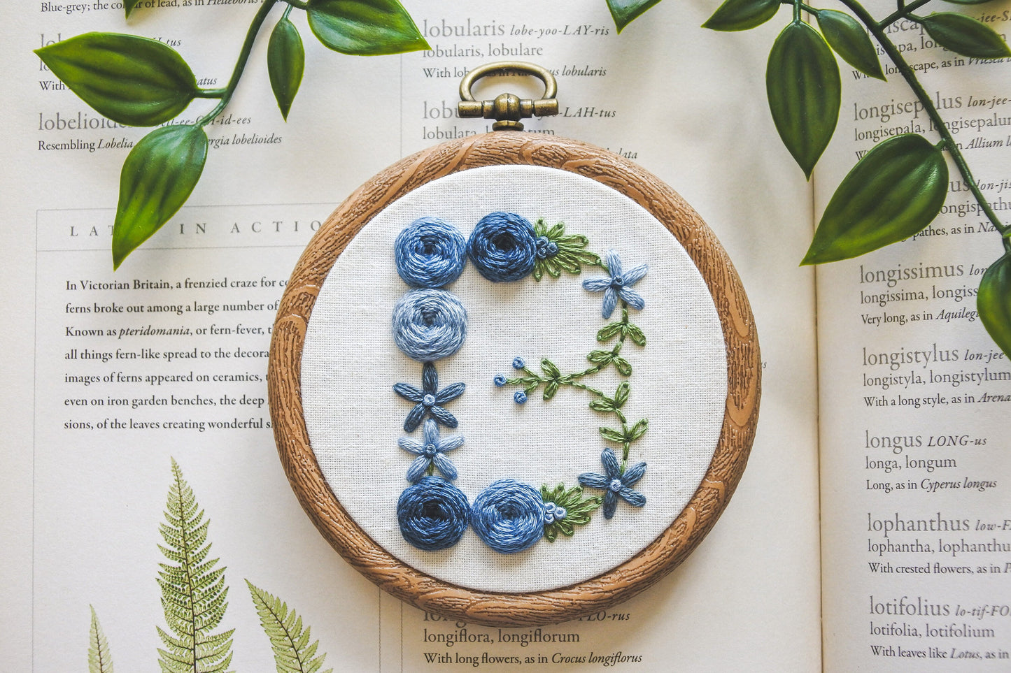 Blue floral letter 'B' embroidery hoop, showcasing the delicate floral details and green foliage.