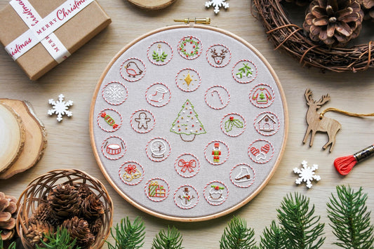 Flatlay of hand embroidered Christmas advent calendar design, featuring festive mini motifs stitched in red and white candy cane circles around a Christmas tree.