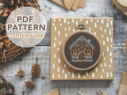 Hand-embroidered gingerbread house design on brown fabric, featuring leaf and heart icing accents. Includes text "PDF pattern and stitch guide."