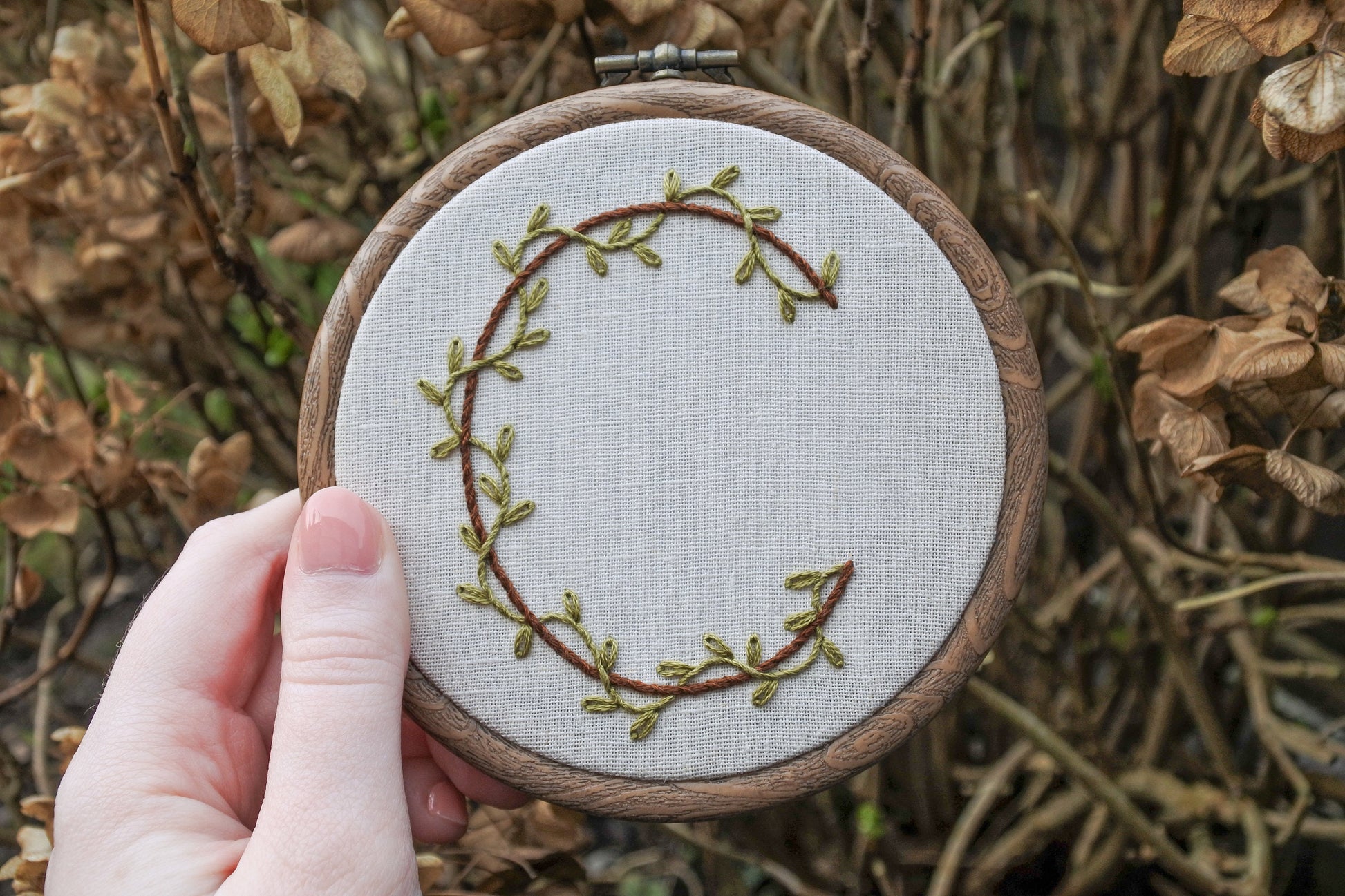 Hand holding botanical letter c embroidery hoop art