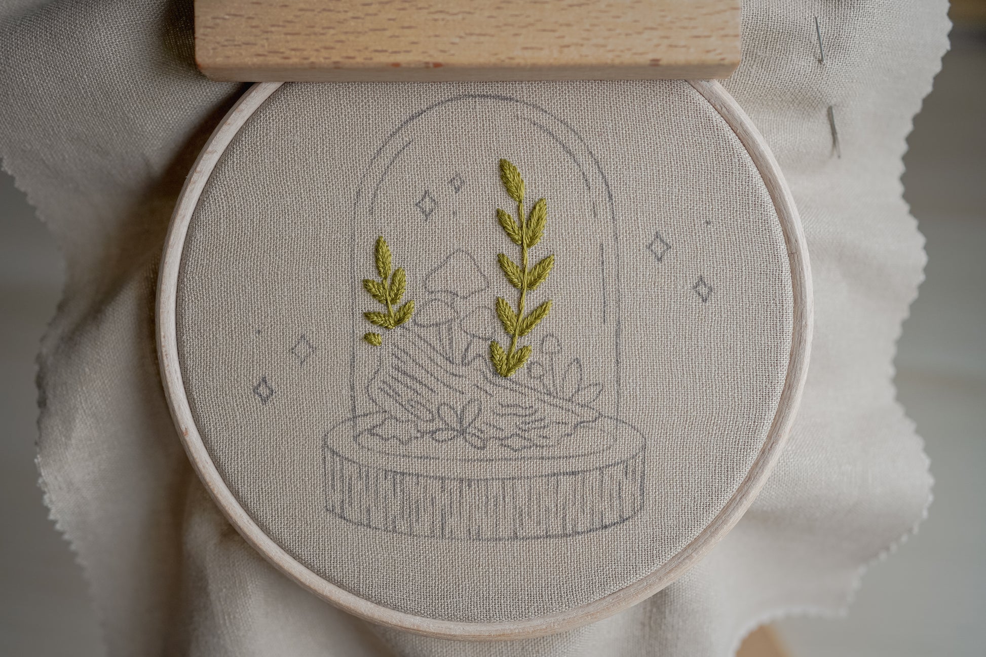Embroidery hoop with embroidered design of leafy green foliage on a light fabric background.