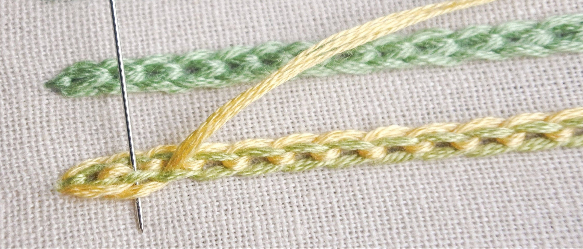 Close-up of interlaced chain stitch in progress, showing the braided detail in lime green and lemon yellow thread