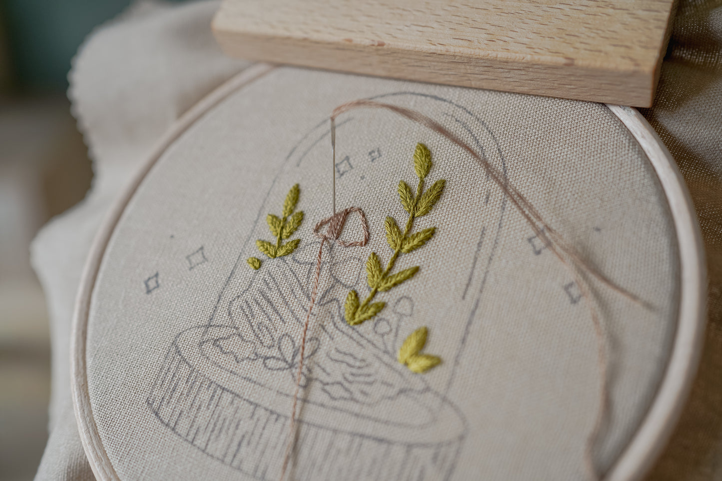 Embroidery hoop with a partially completed mushroom design on light fabric