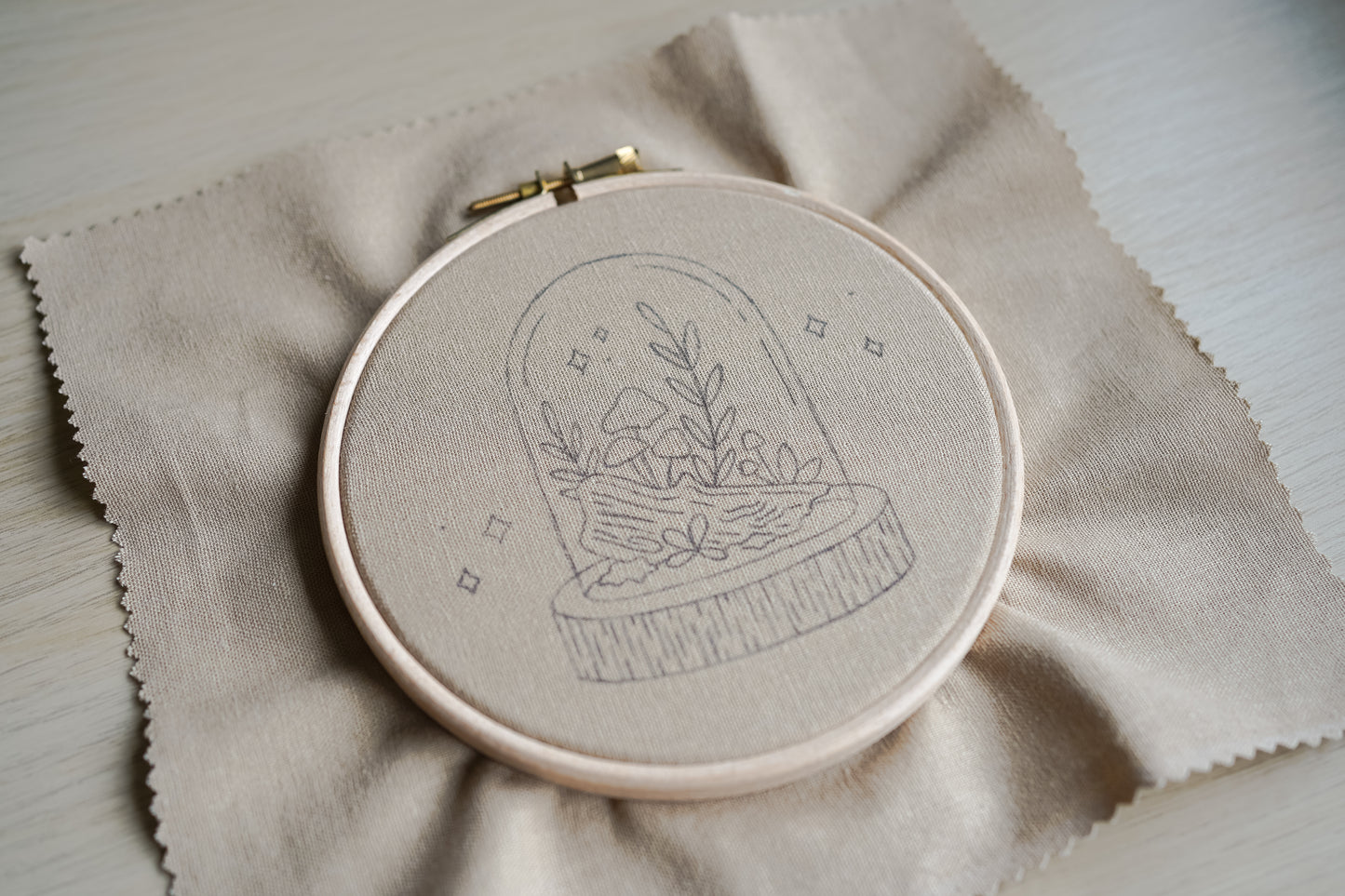 Embroidery hoop with woodland mushroom terrarium design drawn on a beige fabric background