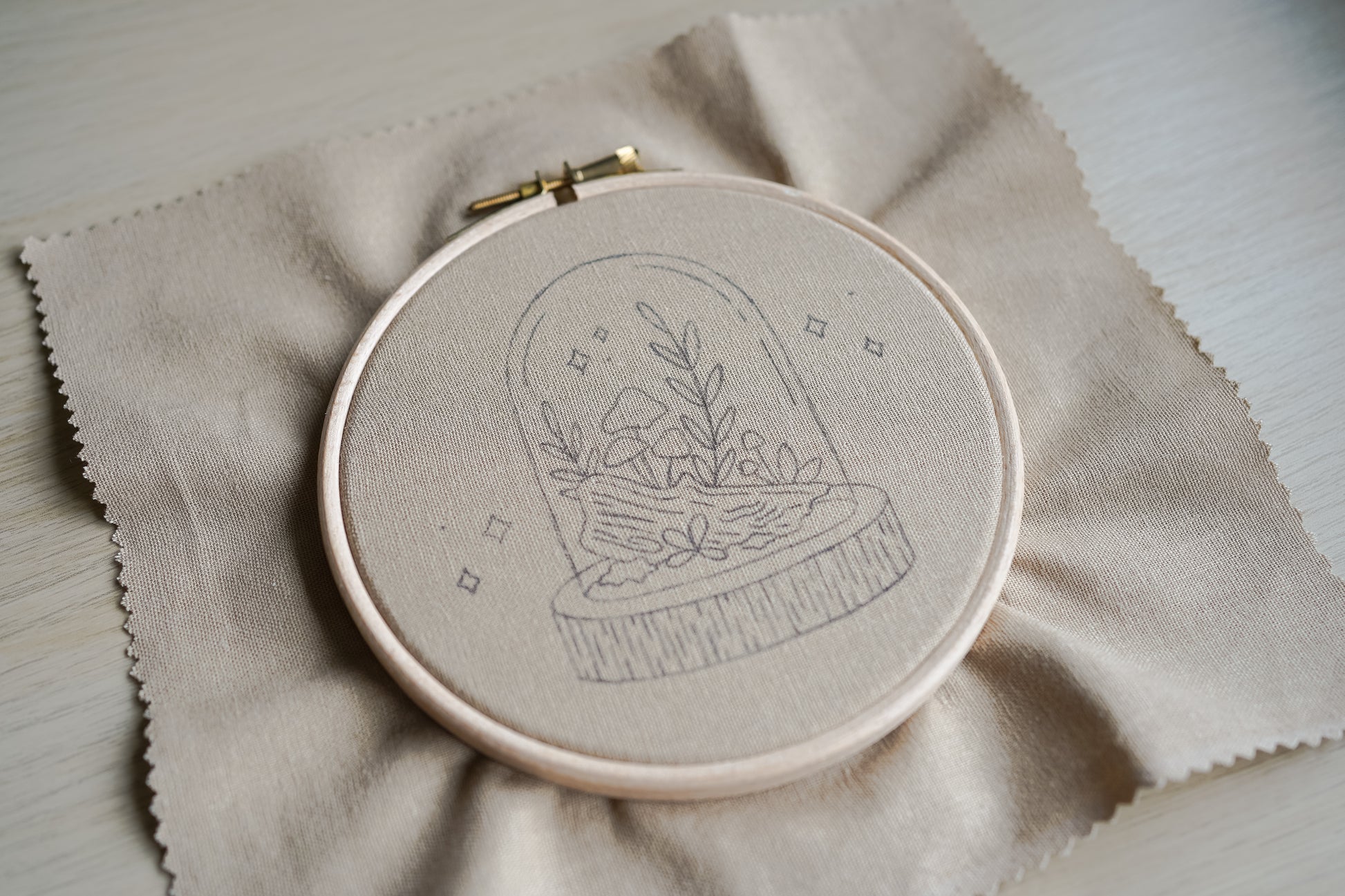 Embroidery hoop with woodland mushroom terrarium design drawn on a beige fabric background