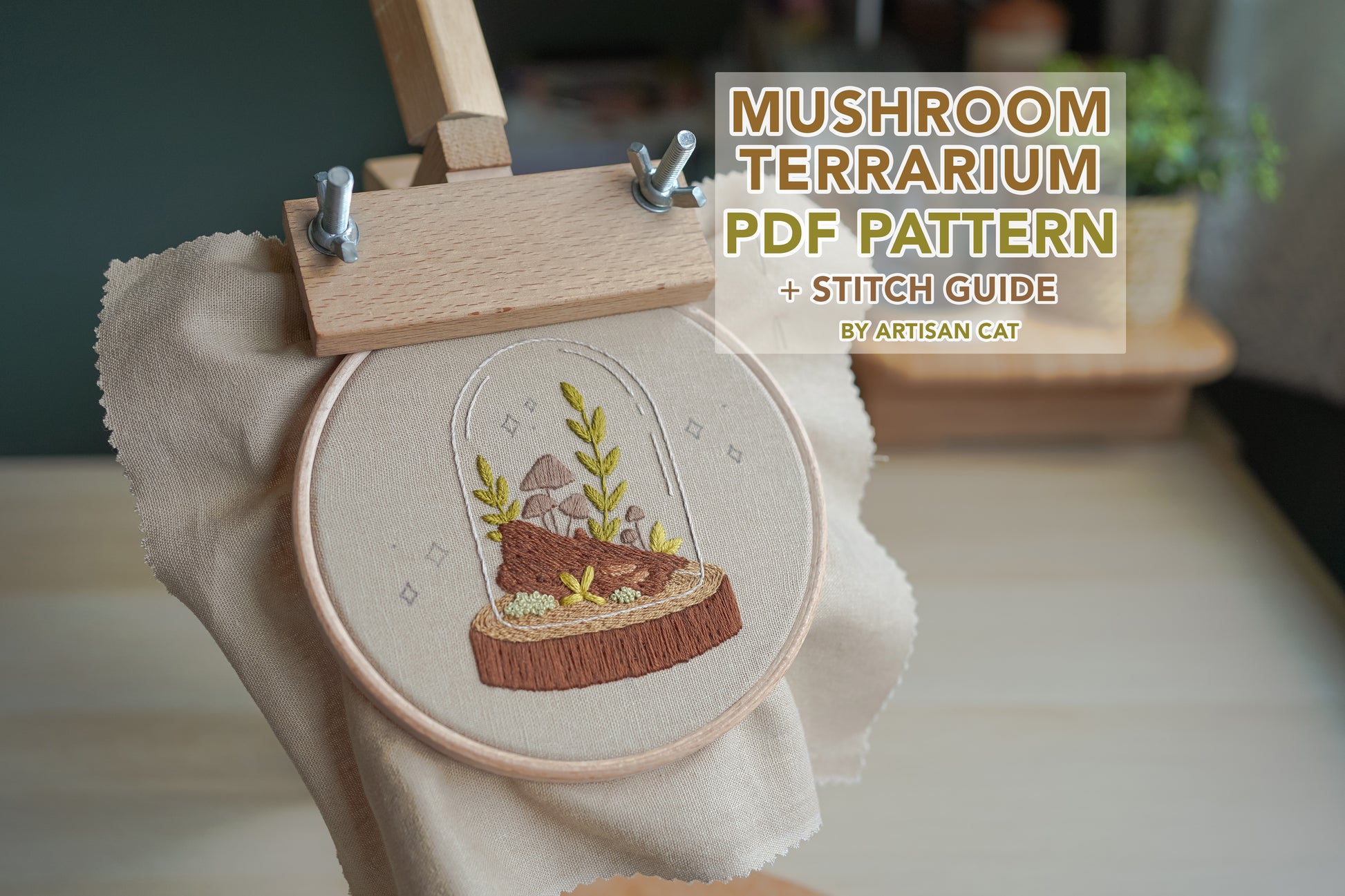 Woodland mushroom terrarium hand embroidery displayed in a wooden hoop stand, with text reading “mushroom terrarium PDF pattern and stitch guide by artisan cat”. Nature-inspired cosy crafting design.