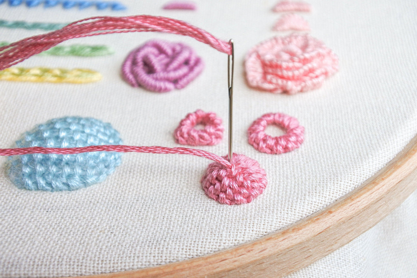 Close-up of needle stitching a raised cup stitch in pink thread on fabric
