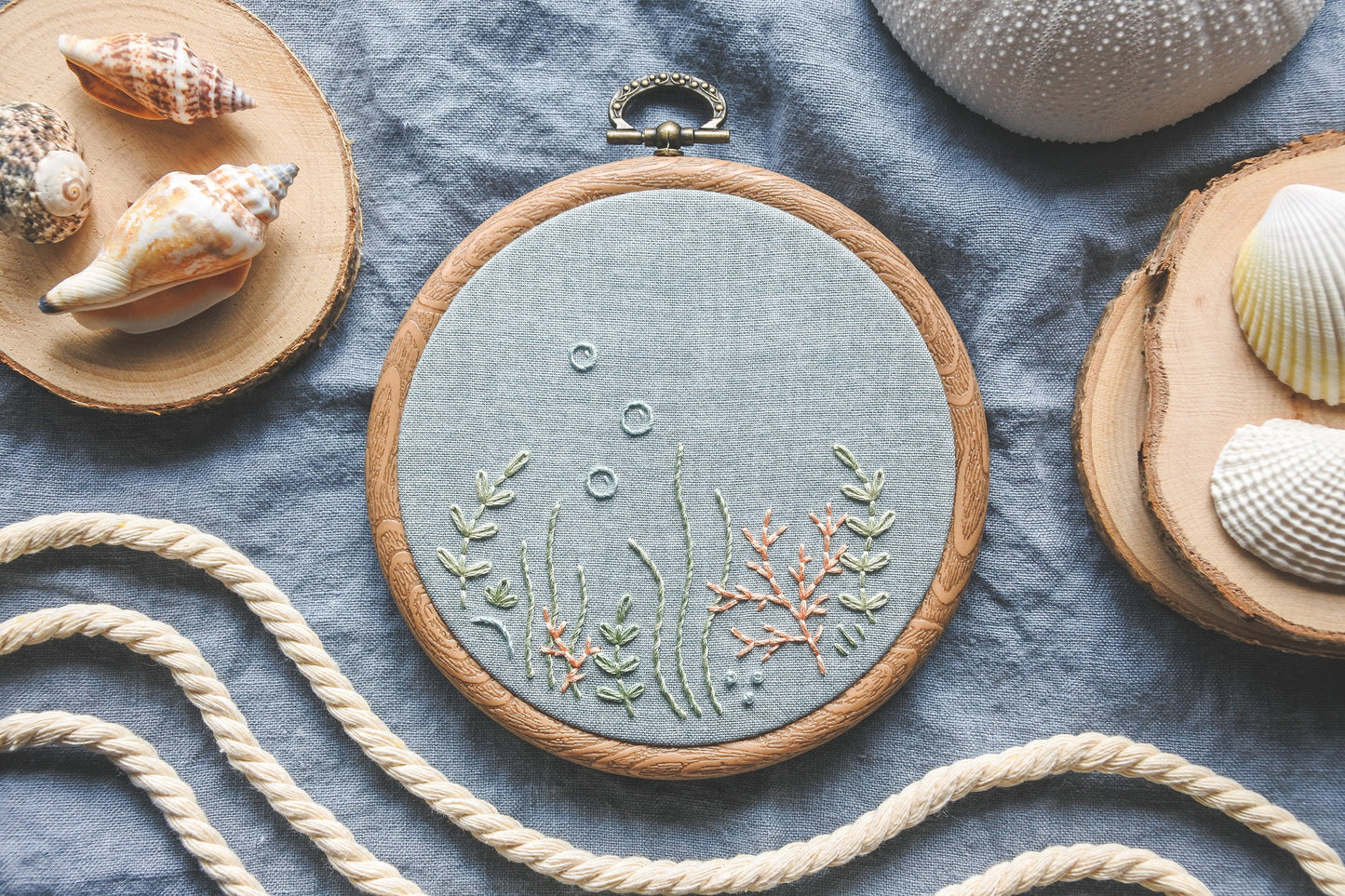 Hand-embroidered coral reef design on light blue fabric in wood effect hoop