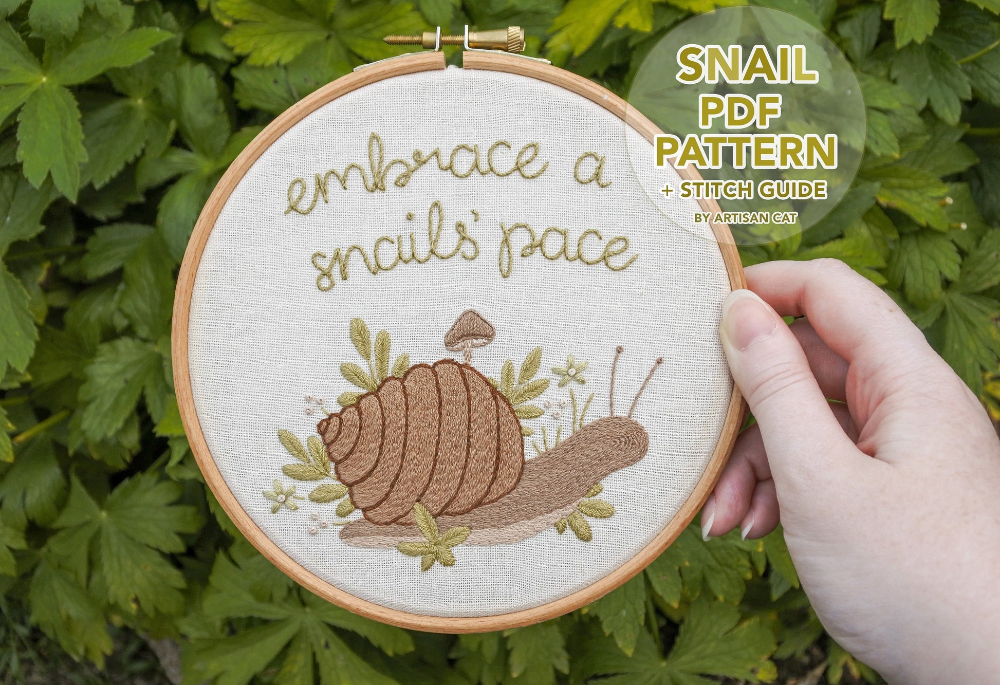 Hand holding the snail embroidery hoop with text overlay in a bubble saying 'Snail PDF Pattern and Stitch Guide by Artisan Cat'