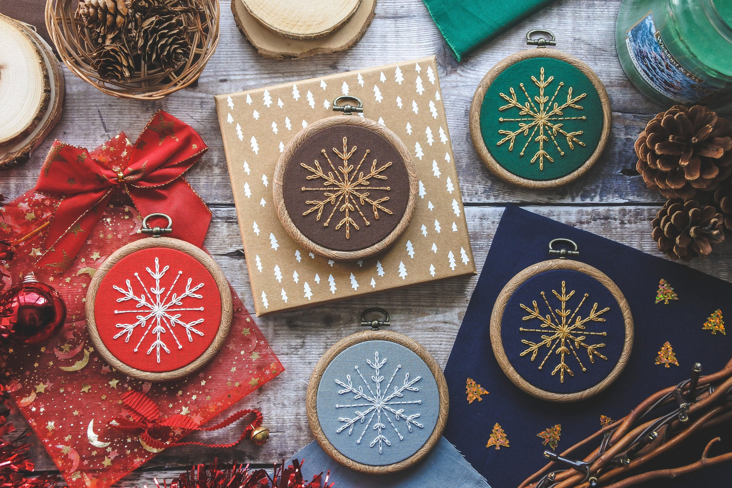Flatlay showing five 3-inch embroidery hoops with snowflake designs in different colours including red, brown, green, dark blue and light blue.