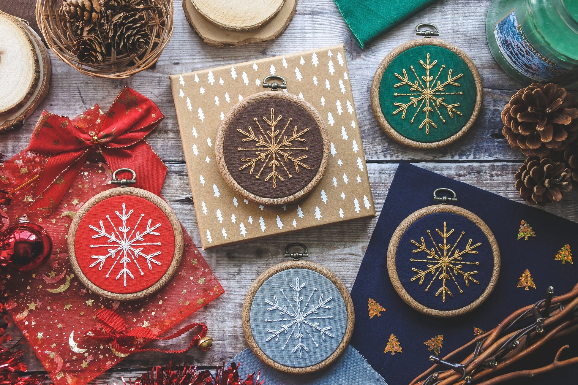 Flatlay showing five 3-inch embroidery hoops with snowflake designs in different colours including red, brown, green, dark blue and light blue.