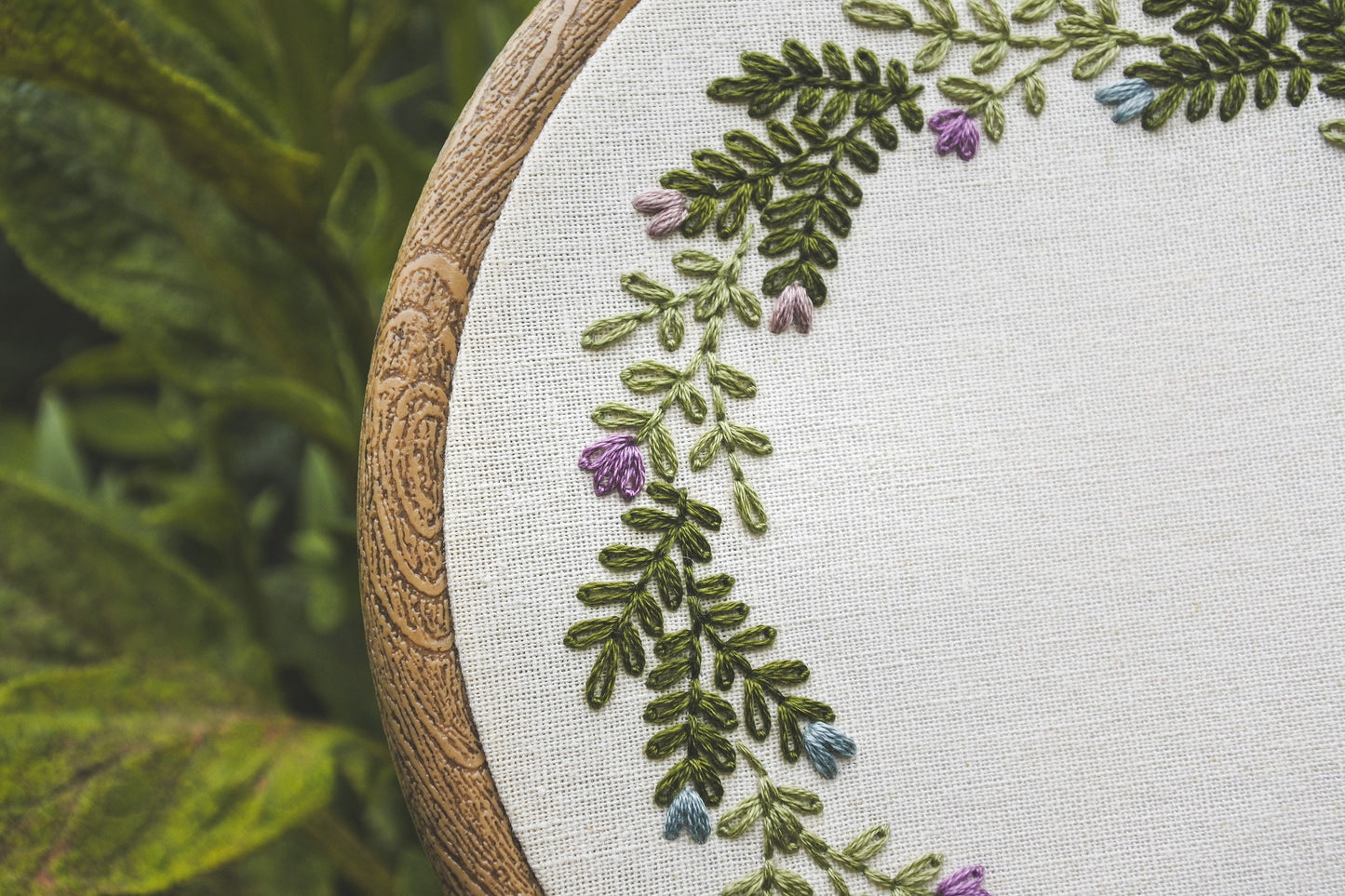Closeup of embroidered  muted blue and purple spring flowers and green foliage details on personalised wreath hoop