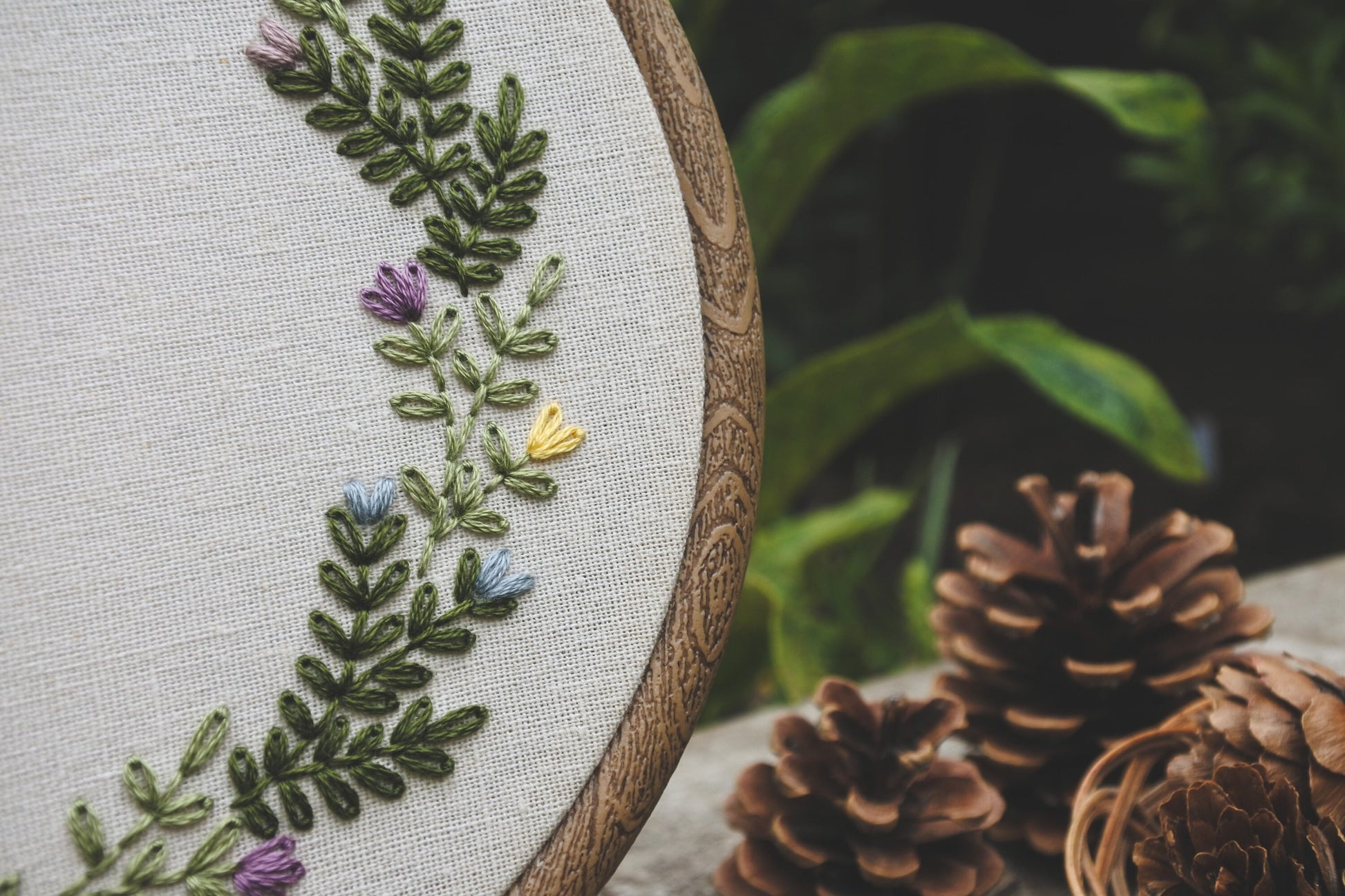 Detail view of hand stitched green foliage and spring flowers on personalised embroidery hoop