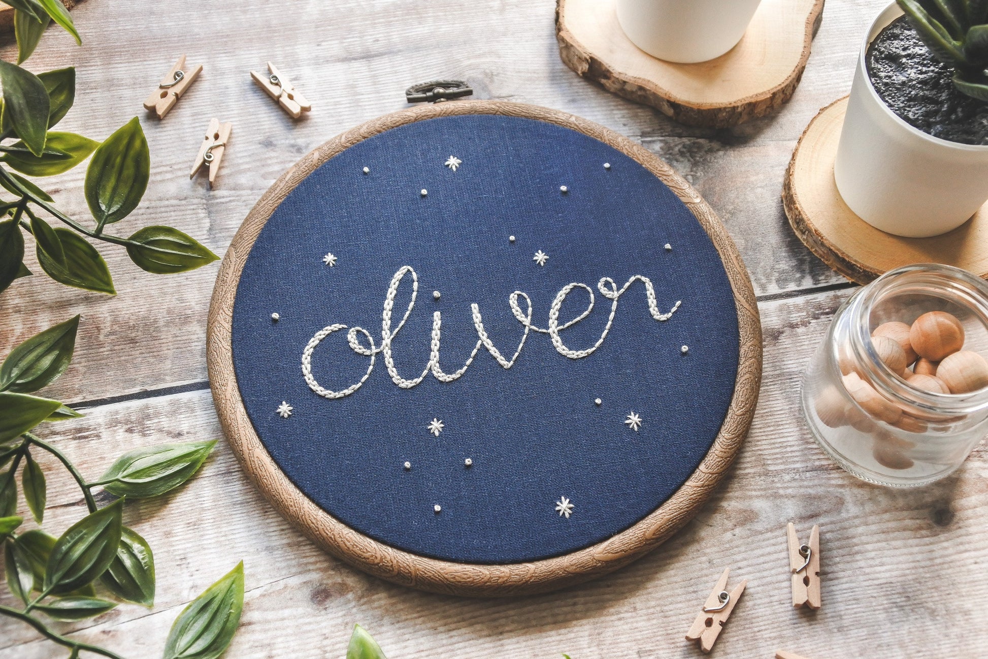 Hand embroidered name 'Oliver' surrounded by white stars on navy blue fabric in a wood-effect hoop