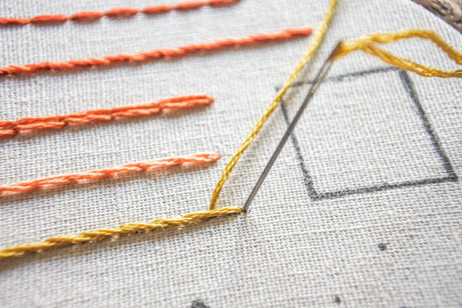 Closeup of stem stitch embroidery in progress, using yellow thread.