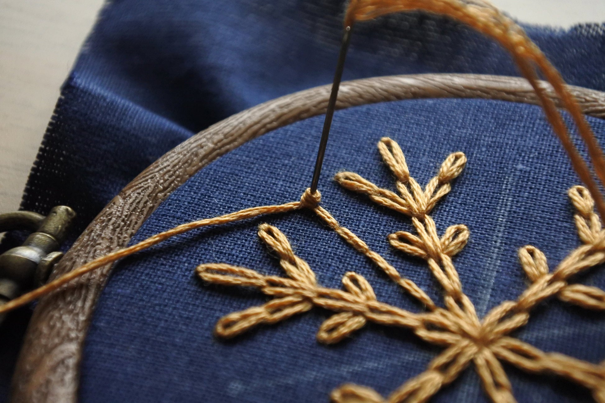 Needle stitching a gold French knot on navy blue fabric
