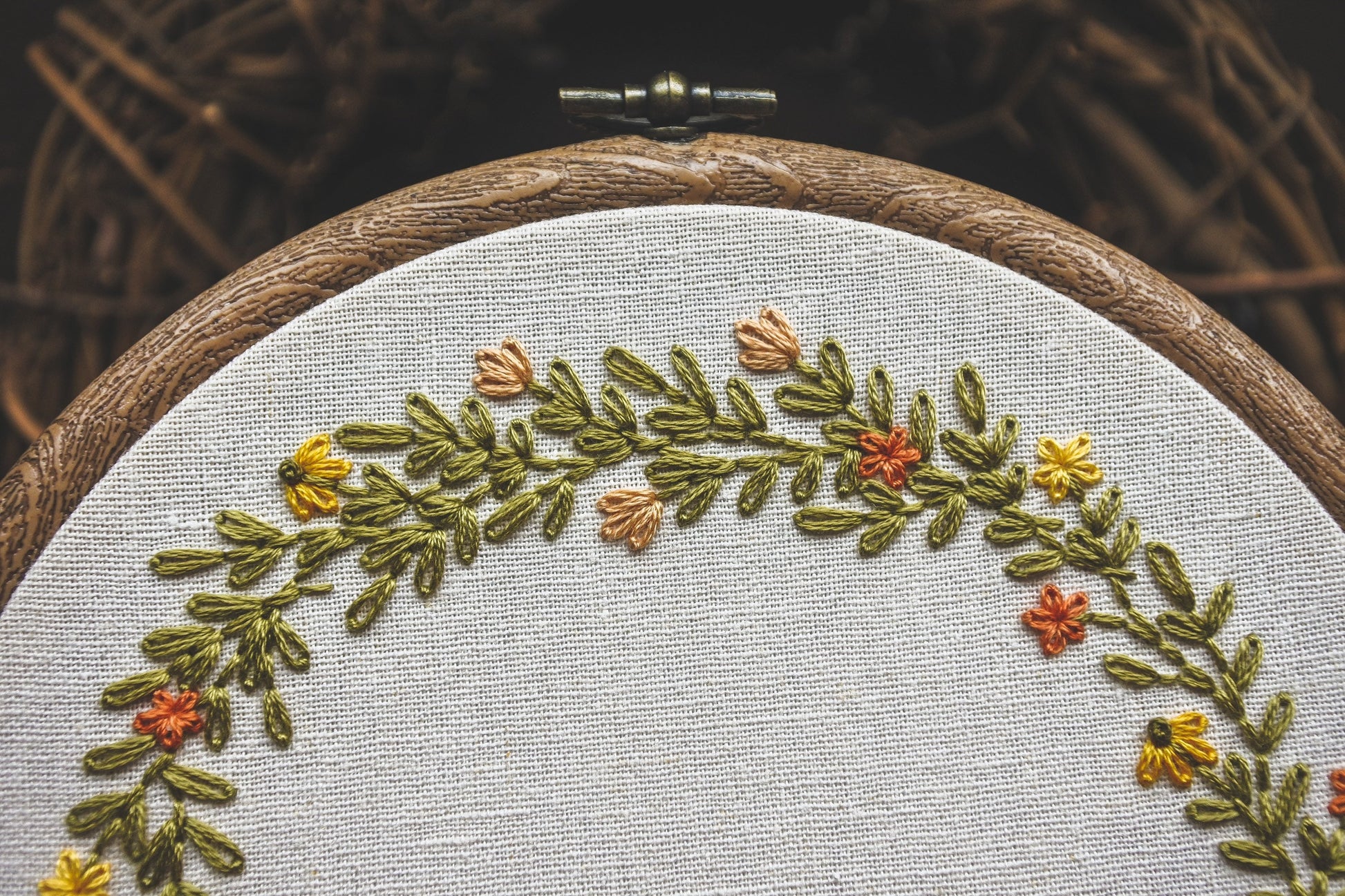 Detail view of the hand stitched name Bella framed by vibrant summer flowers and foliage