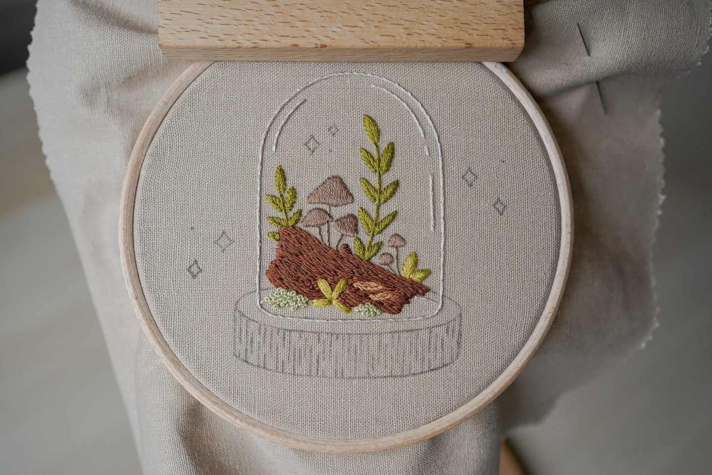 Embroidery hoop with a nature-themed embroidery design featuring mushrooms and plants on a neutral background